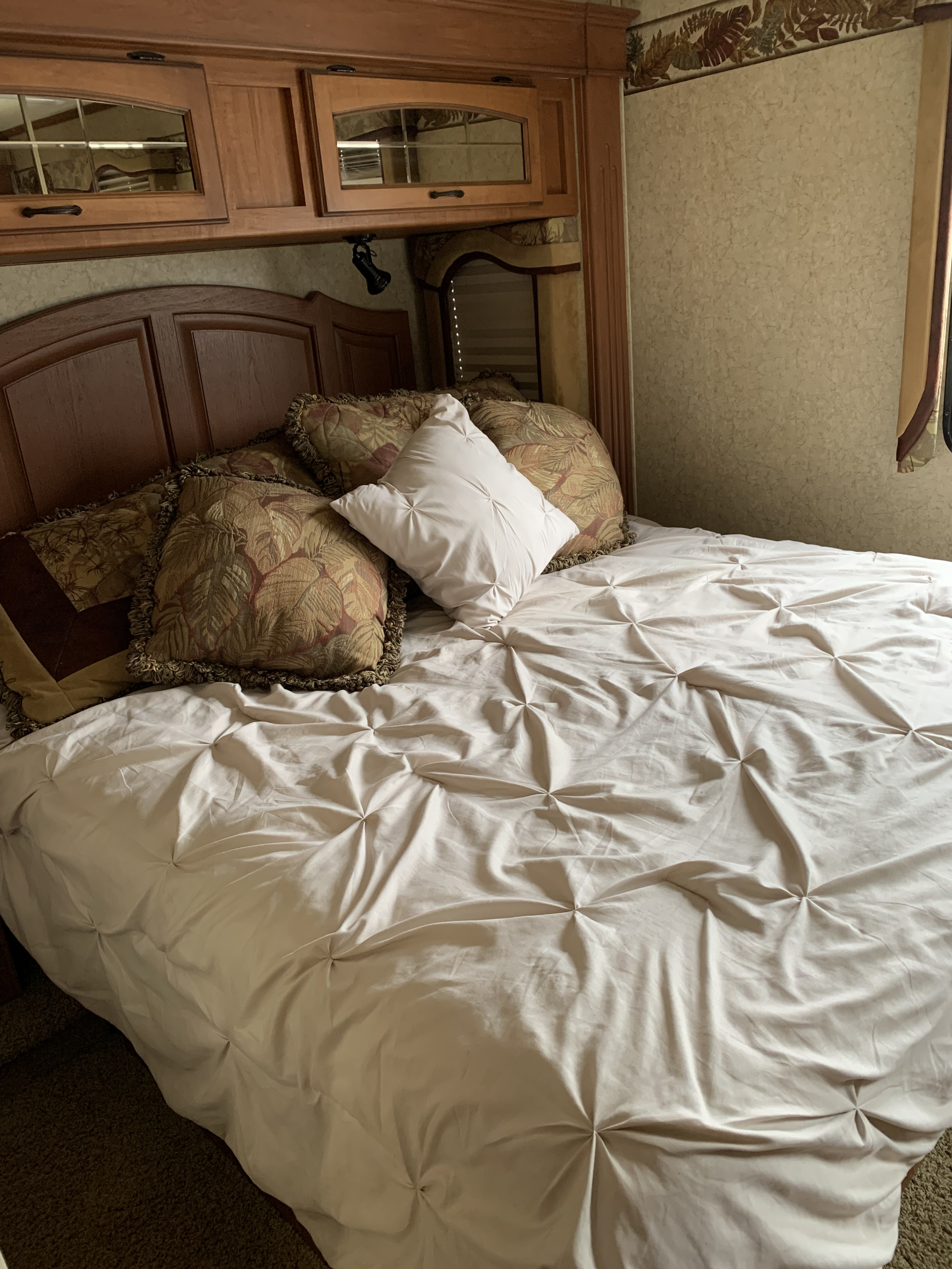 Cozy RV rental bedroom with a bed, patterned pillows, light tufted comforter, and overhead wooden cabinets.. Jayco Seneca HD 2007