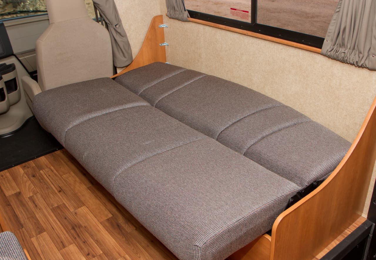 Inside an RV rental, a plush gray convertible bed provides flexible sleeping and seating in this compact camper interior.. Thor Majestic 2015