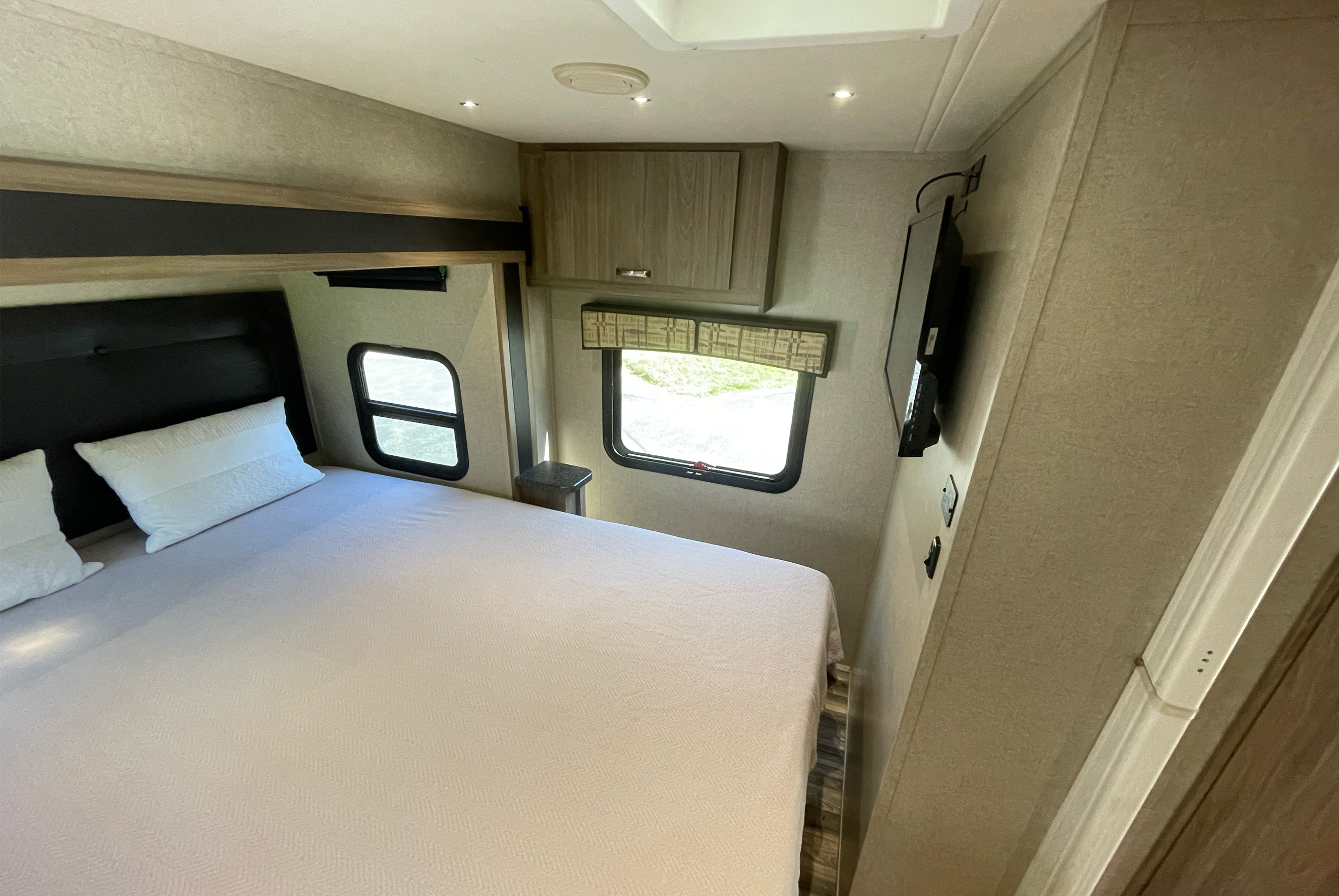 This RV rental bedroom offers a comfortable bed, two windows for natural light, overhead storage, and a mounted TV.. Isata 3 2017