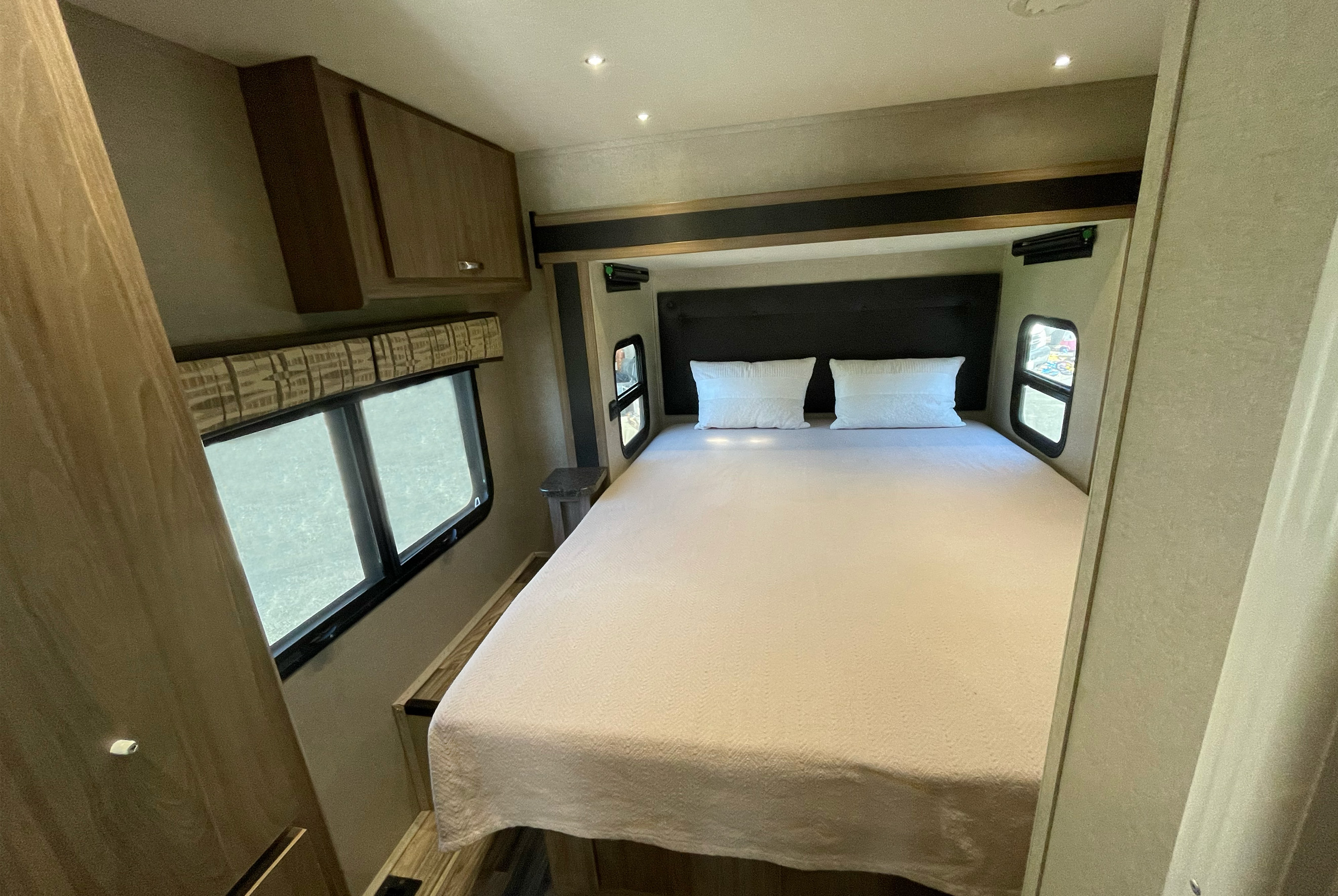 Cozy RV rental bedroom featuring a comfortable queen bed, overhead cabinets, and windows on both sides.. Isata 3 2017