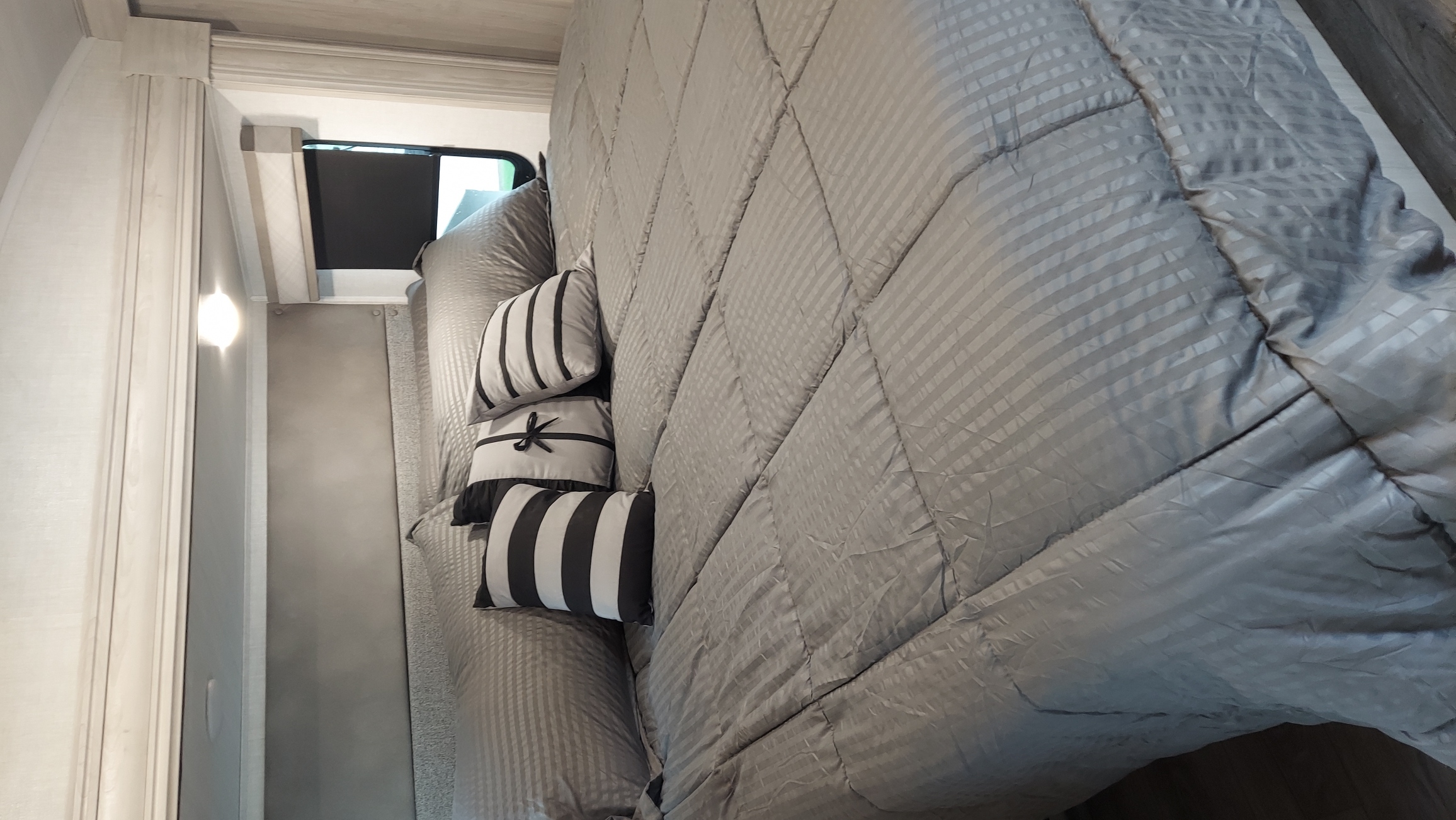 Comfortable RV rental bedroom featuring a gray striped comforter and black & white decorative pillows on the bed.. East to West Tandara 2021