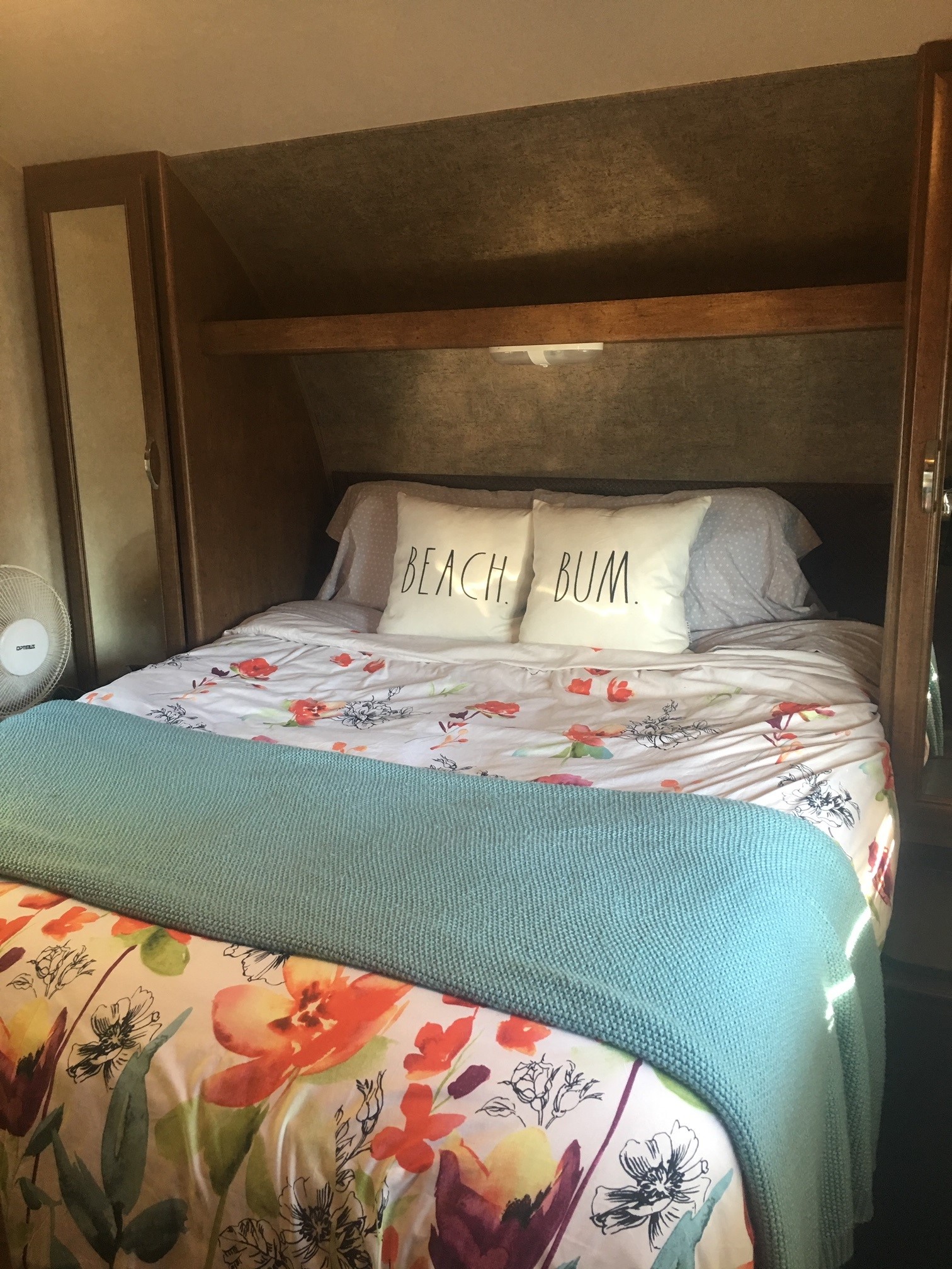 Cozy RV rental bed with floral duvet, "BEACH BUM" pillows, and overhead storage for a comfortable journey.. Forest River Salem 2016