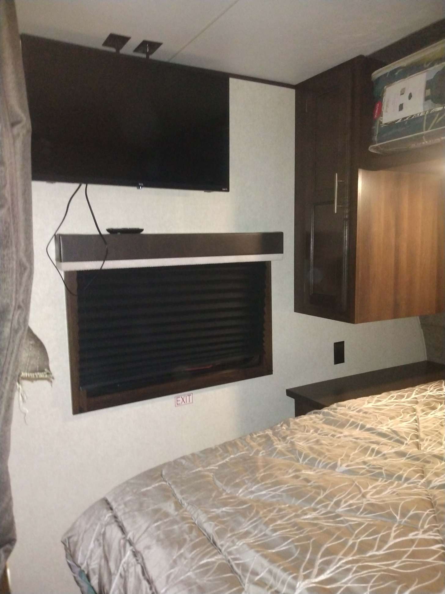 Cozy RV rental bedroom with a wall-mounted TV, window with closed blinds, dark wood cabinets, and patterned bed comforter.. Jayco FLIGHT SLX 2020