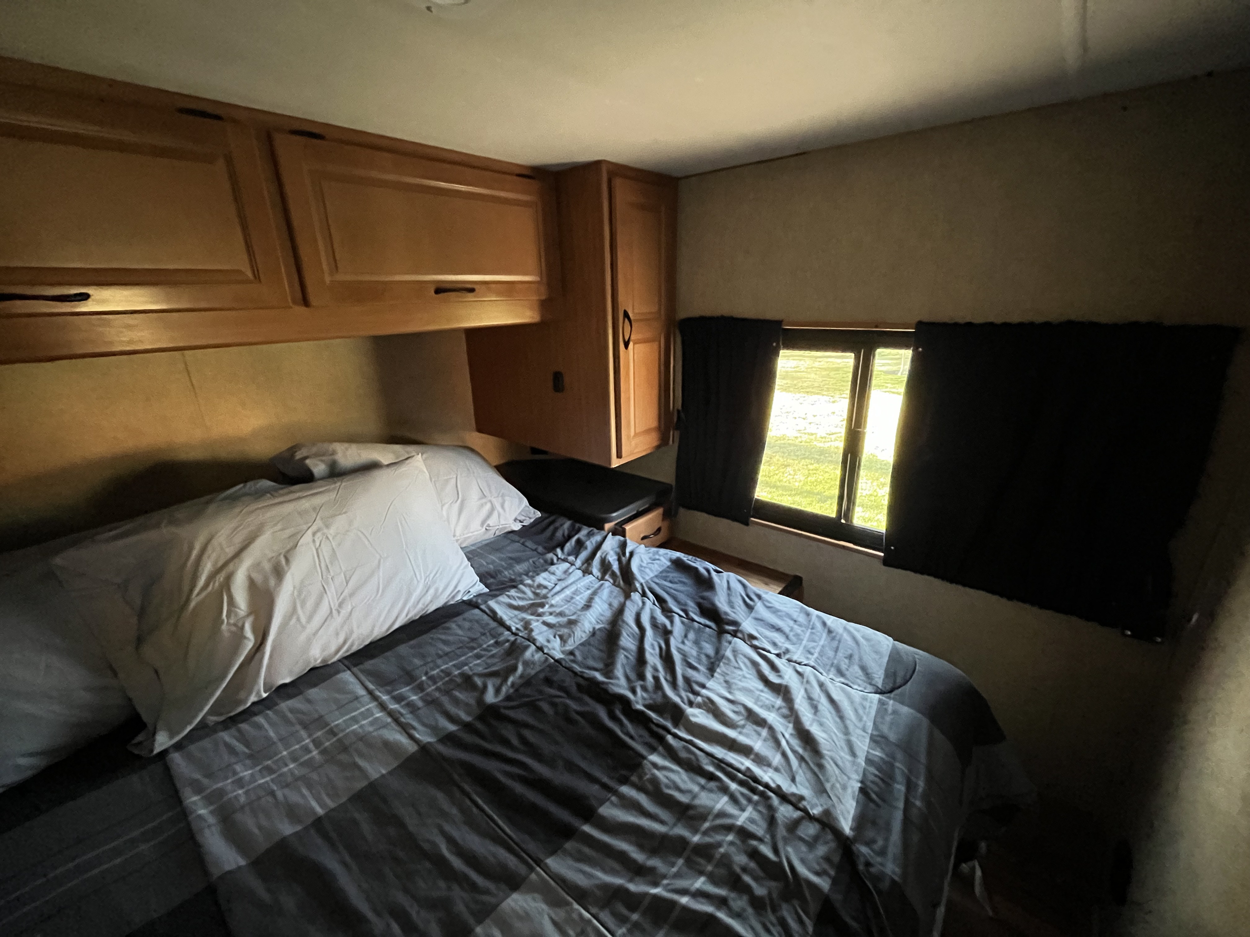 Compact RV rental bedroom featuring a bed, ample wooden cabinets, and a bright window view of nature.. Thor Majestic 2017