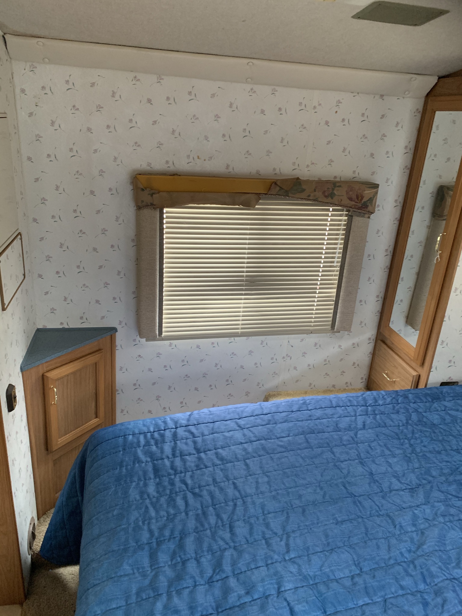 Cozy RV rental bedroom: blue quilted bed, floral walls, window with blinds, and built-in wood cabinetry.. Ford Tioga 1998