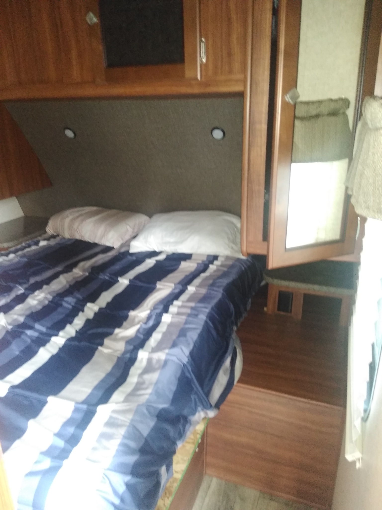 Cozy RV rental bedroom featuring a blue striped bed, white pillows, and wooden overhead storage cabinets.. Heartland RVs Mallard 2017