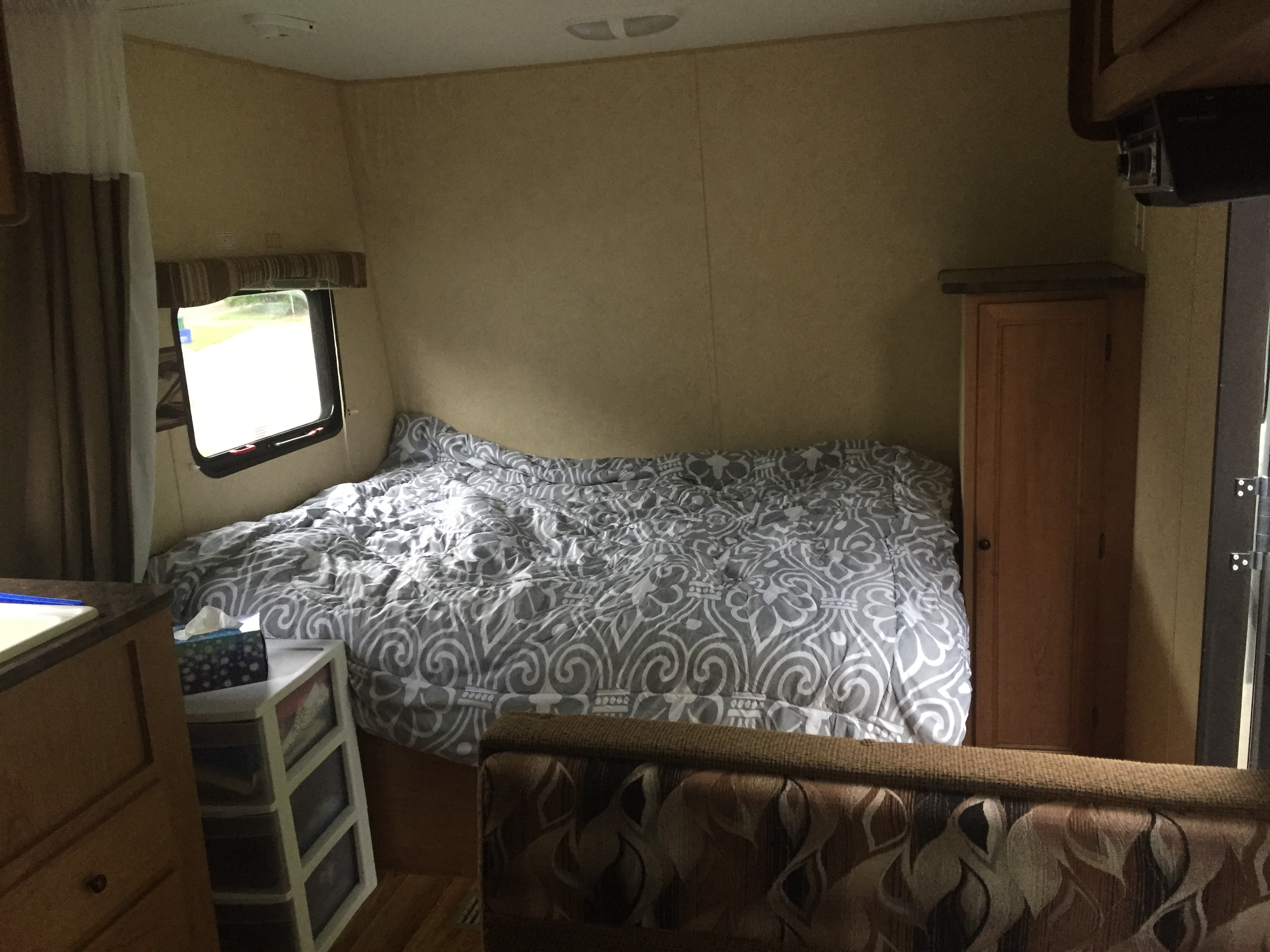 Inside this RV rental: a cozy bedroom with a patterned comforter, window, cabinet, and living area seating.. Bobcat Bobcat Trailer 2013
