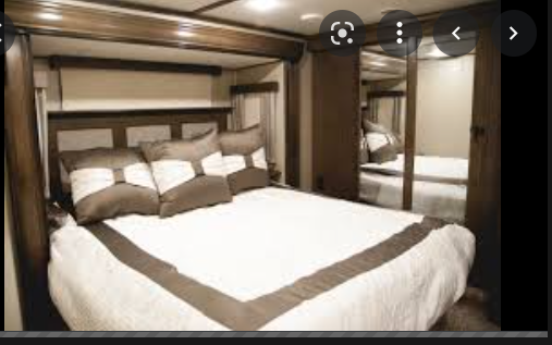 Relax in this RV rental's cozy bedroom. Features a large bed, brown headboard, and mirrored closets for storage.. Grand Design Solitude 2018