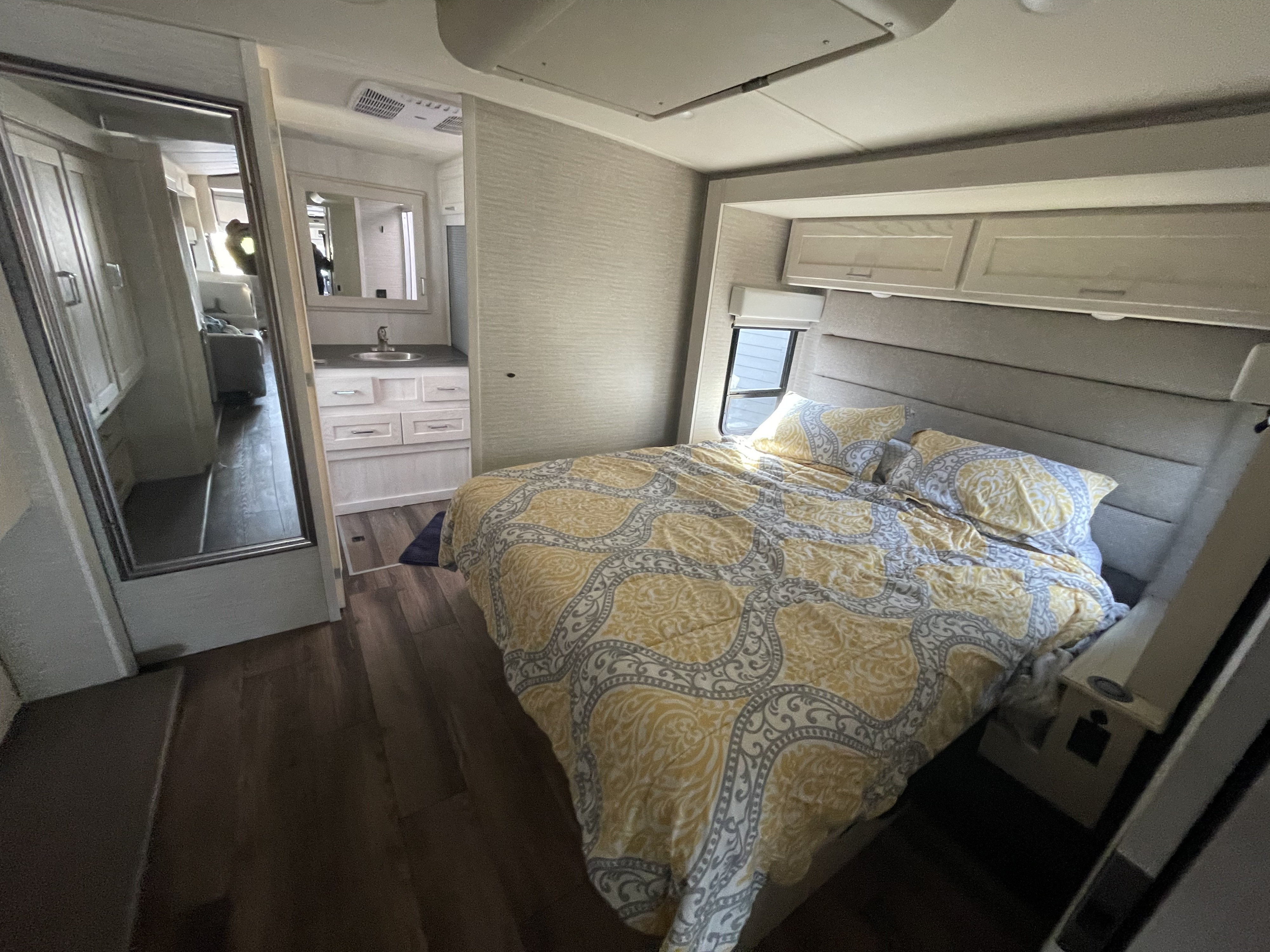 Step into this compact RV rental bedroom featuring a comfy bed with yellow and gray bedding, mirrored closet, and bathroom.. Winnebago Forza 2021