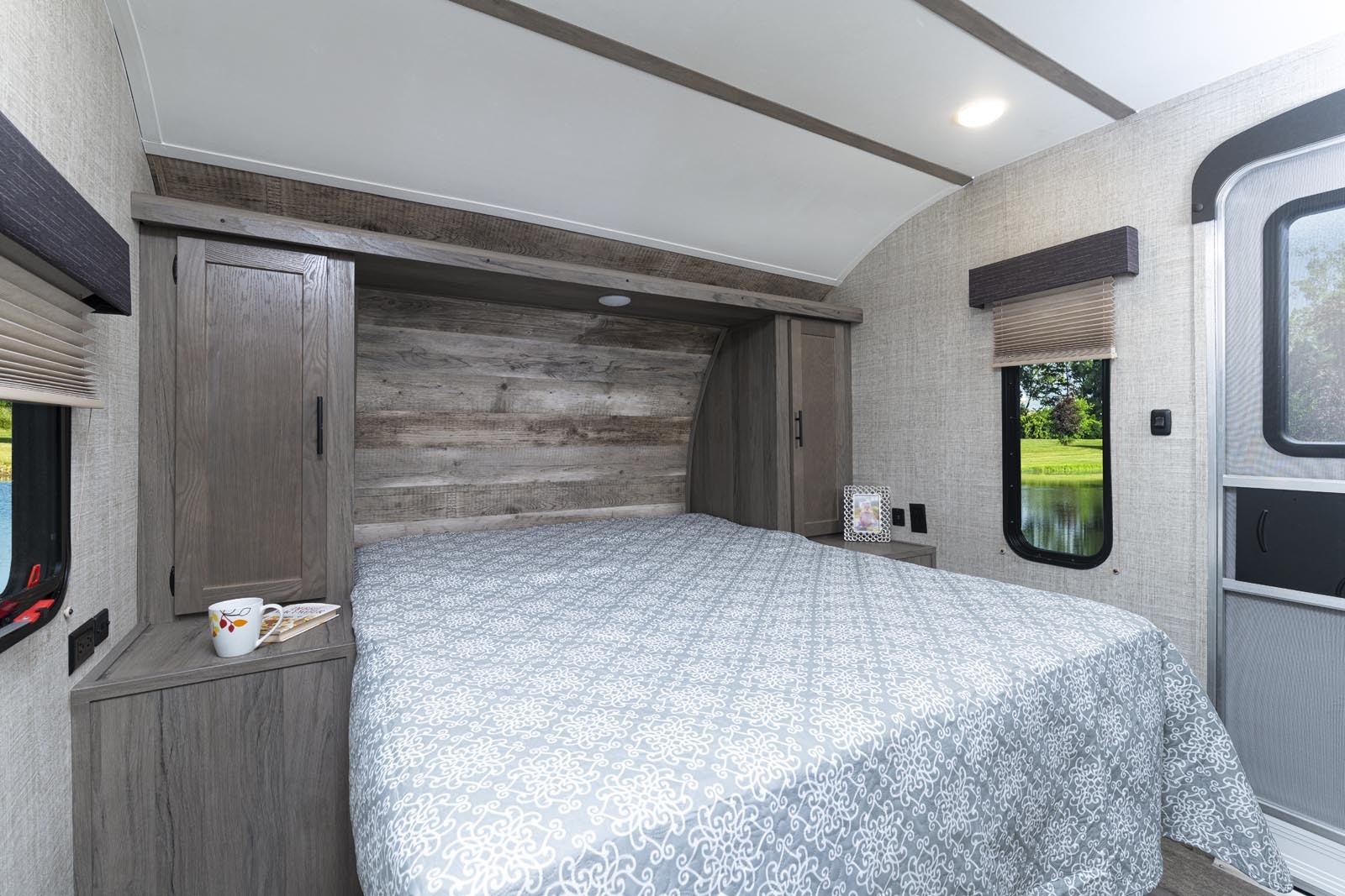 Relax in this cozy RV rental bedroom. Features a comfortable bed, built-in storage, and a picturesque window overlooking a lake.. Gulf Stream Conquest 2021