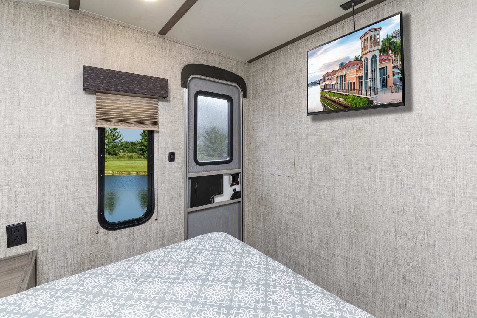 RV rental bedroom interior featuring a patterned bed, window with a lake view, and wall-mounted TV in a compact space.. Gulf Stream Conquest 2021