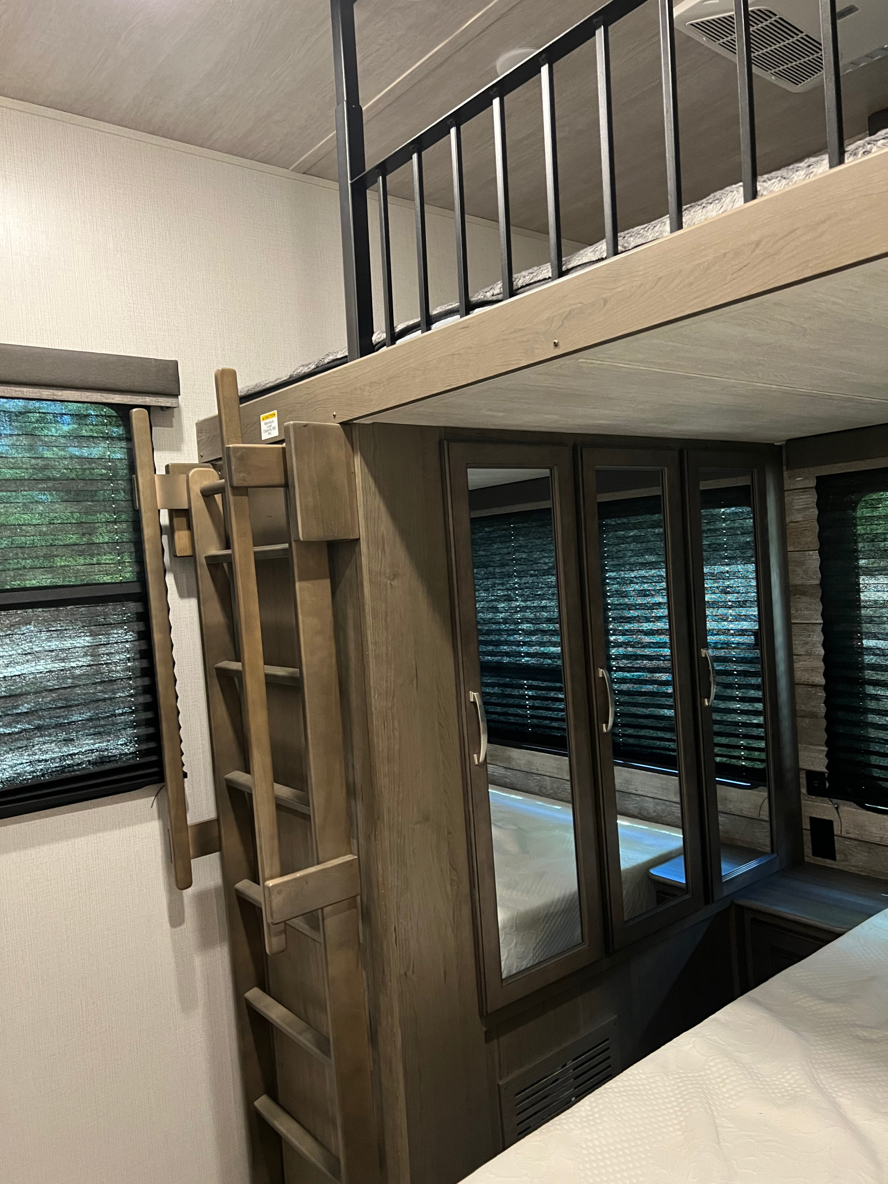 RV rental interior: a comfortable loft bunk bed with ladder, safety railing, and a main bedroom area with mirrored cabinets.. Keystone Cougar 2021