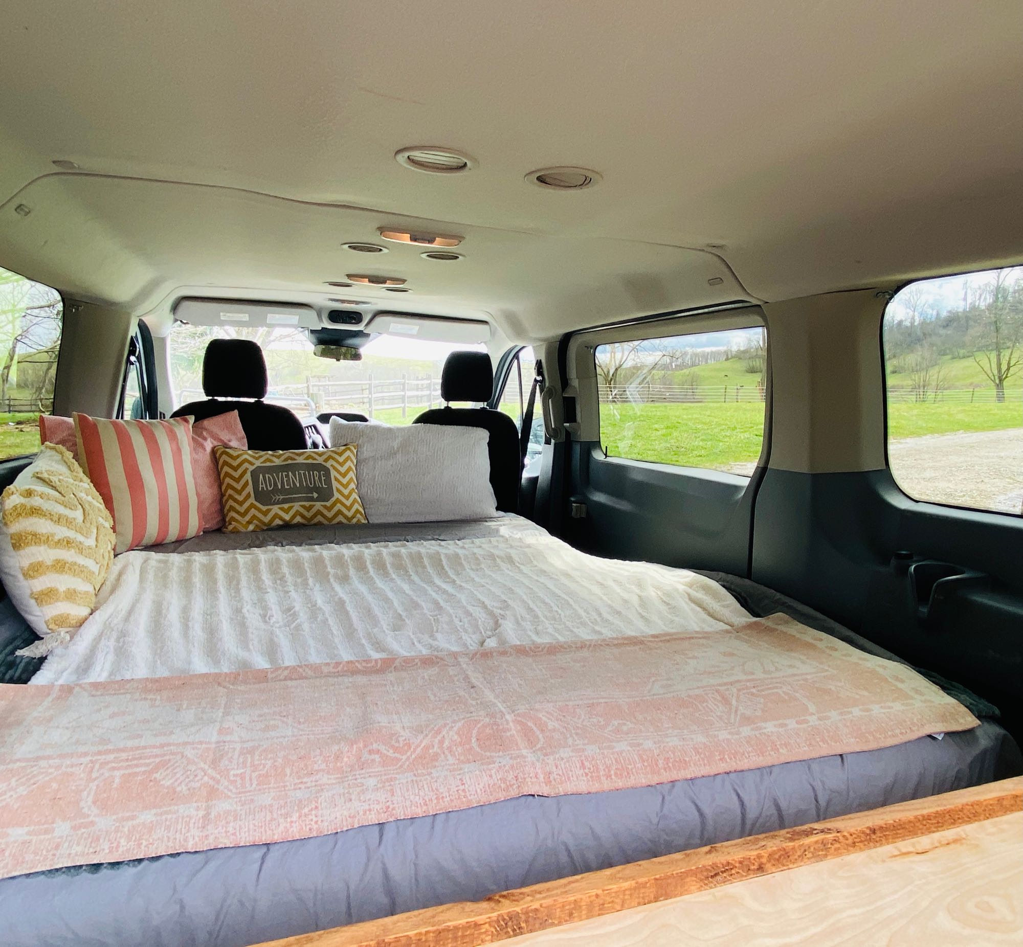 Cozy rv rental van conversion: a comfy bed with striped & "ADVENTURE" pillows, set for mobile living & scenic views.. Ford Transit 2015