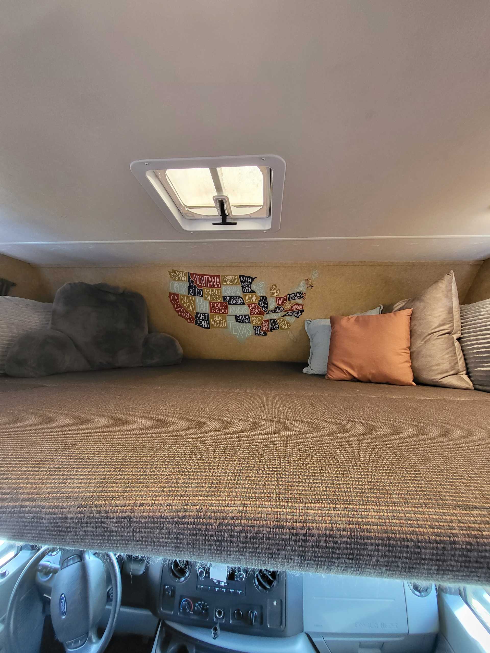 Overhead sleeping area in an RV rental, featuring a US state map, skylight, and cozy pillows for road trip adventures.. Thor Majestic 2014