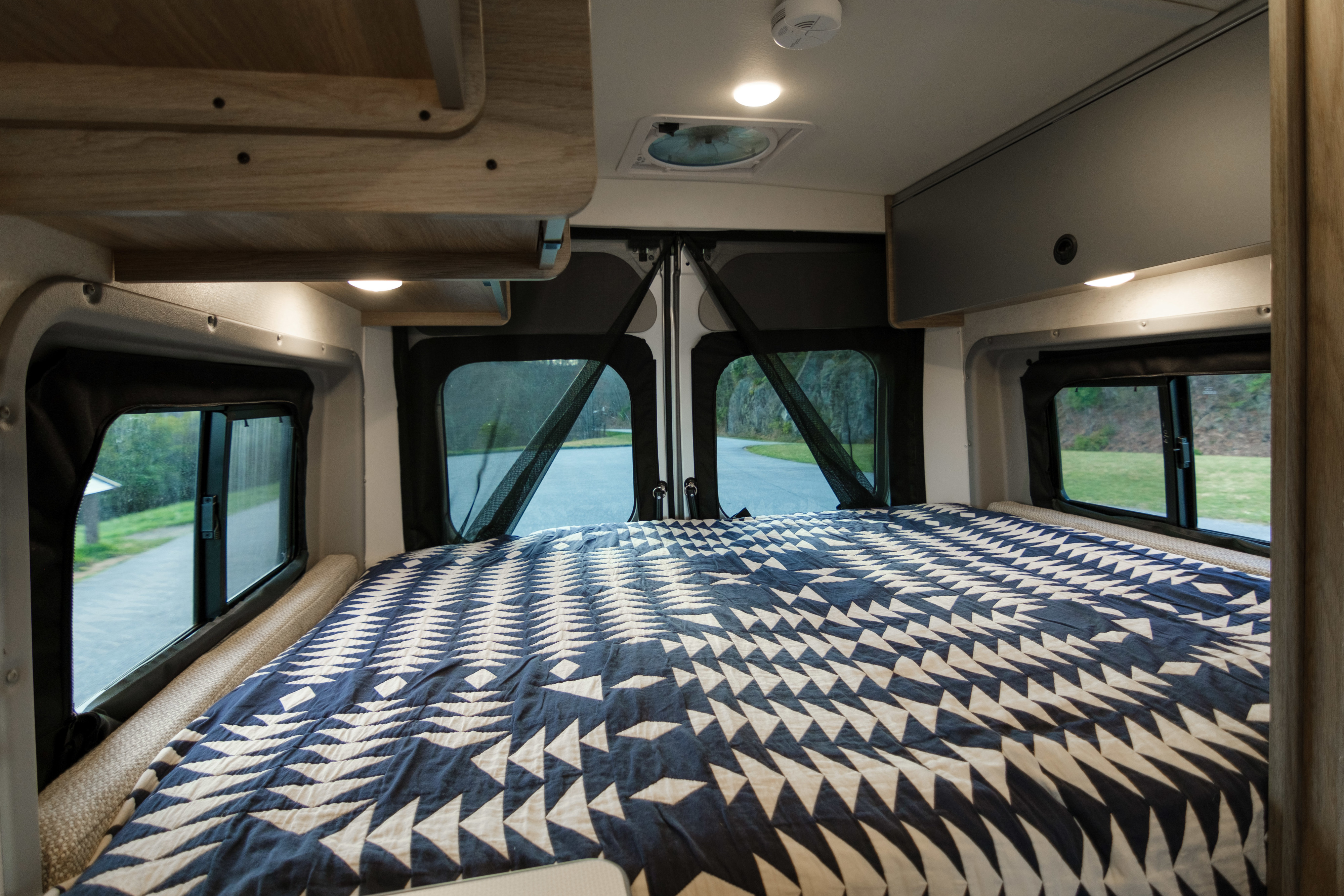 Cozy rv rental bedroom features a geometric blue/white quilt, panoramic windows, and storage for road trip comfort.. Winnebago Solis 2022