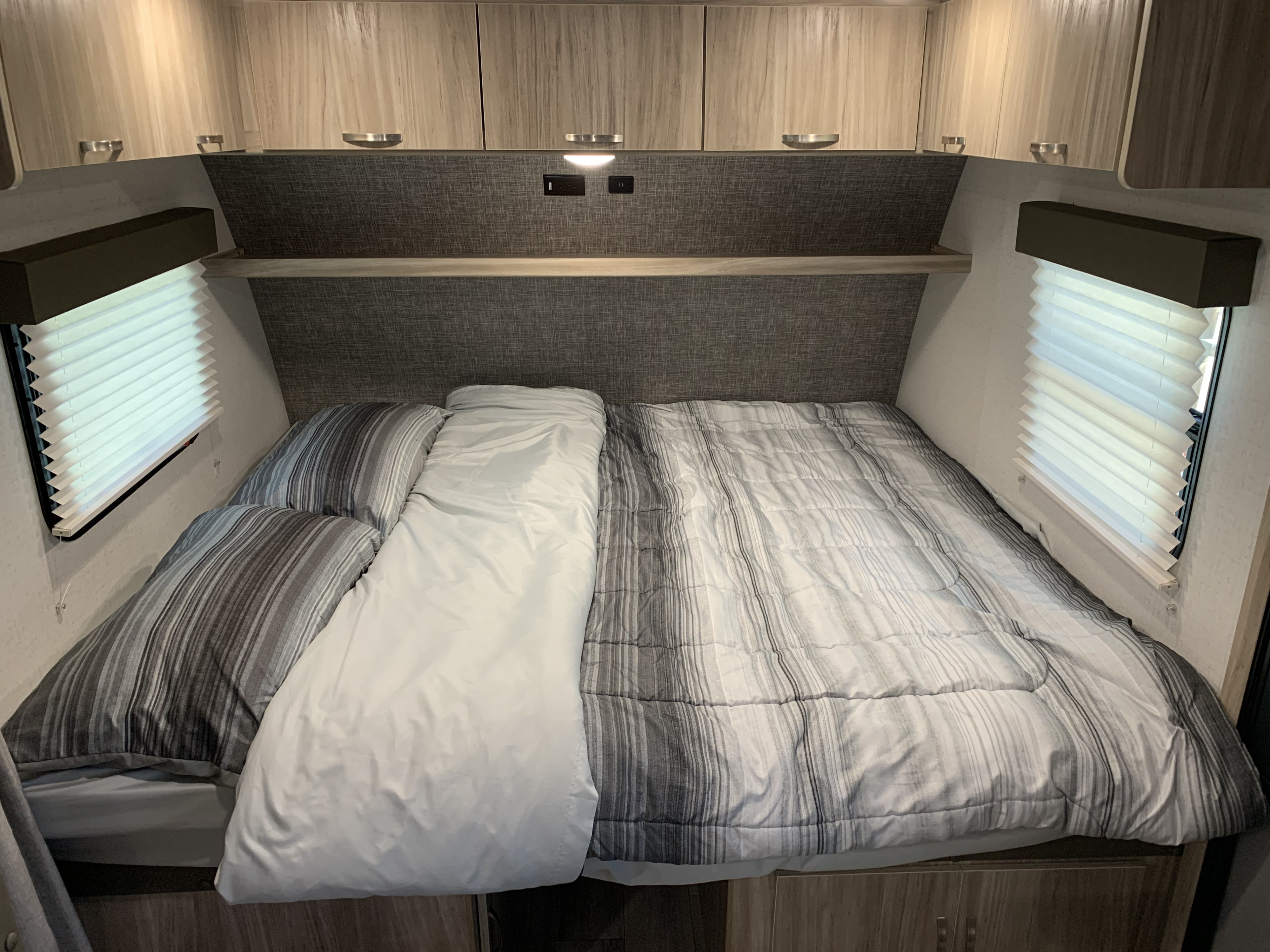 Cozy RV rental bedroom with a bed featuring striped bedding, overhead cabinets, and window blinds.. Winnebago Minnie Winnie 2022