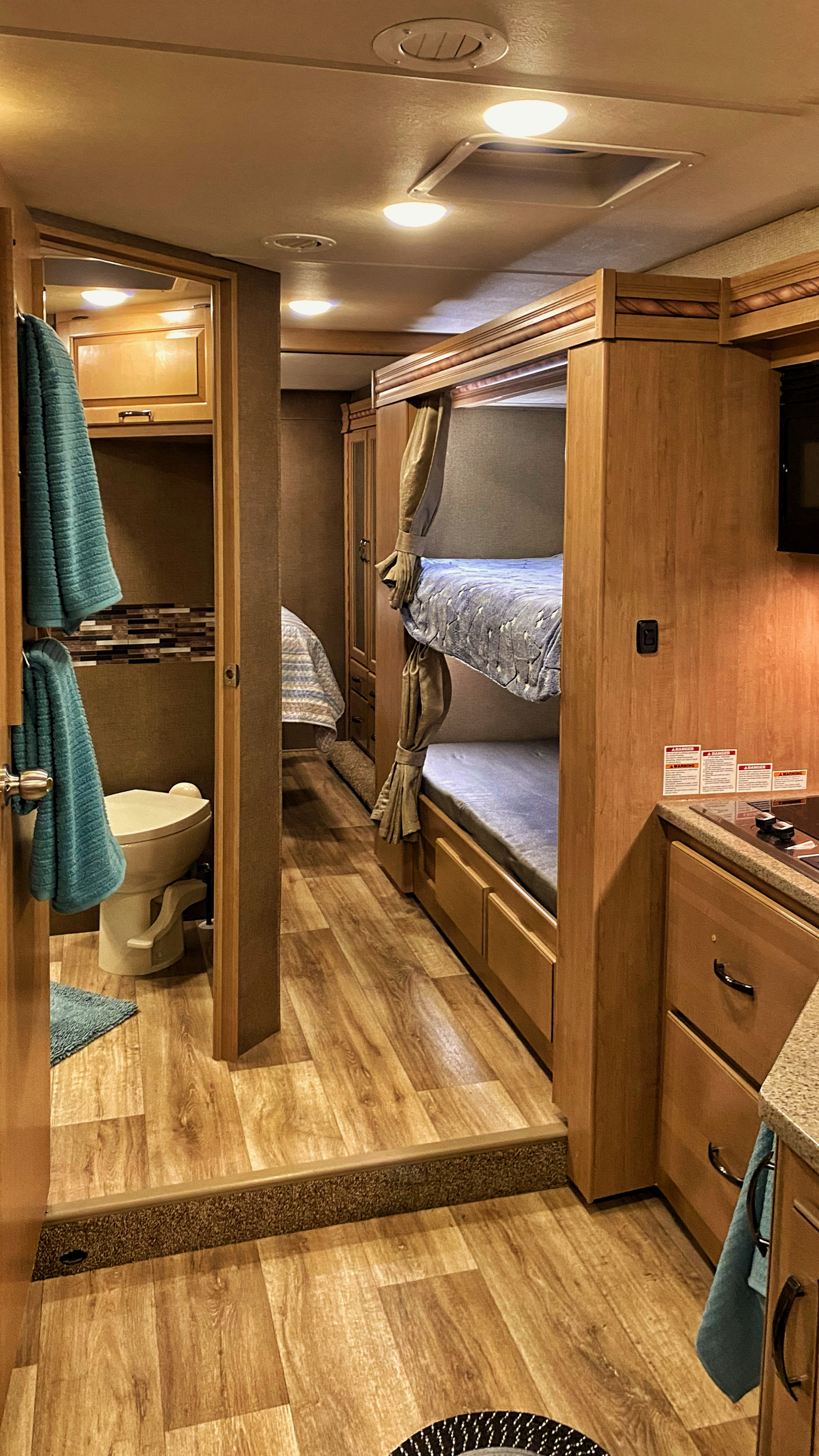 Inside an rv rental, a detailed view of its practical interior: bathroom, bunk beds, and kitchen area with light wood flooring.. Thor Four Winds 2018