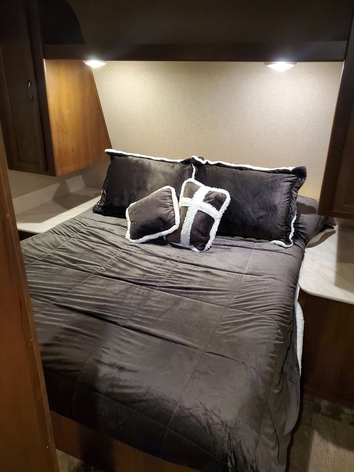 Cozy RV rental bedroom featuring a neatly made bed with dark pillows & comforter. Compact space with overhead lighting.. Jayco Jay Feather Ultra Lite SLX 2015