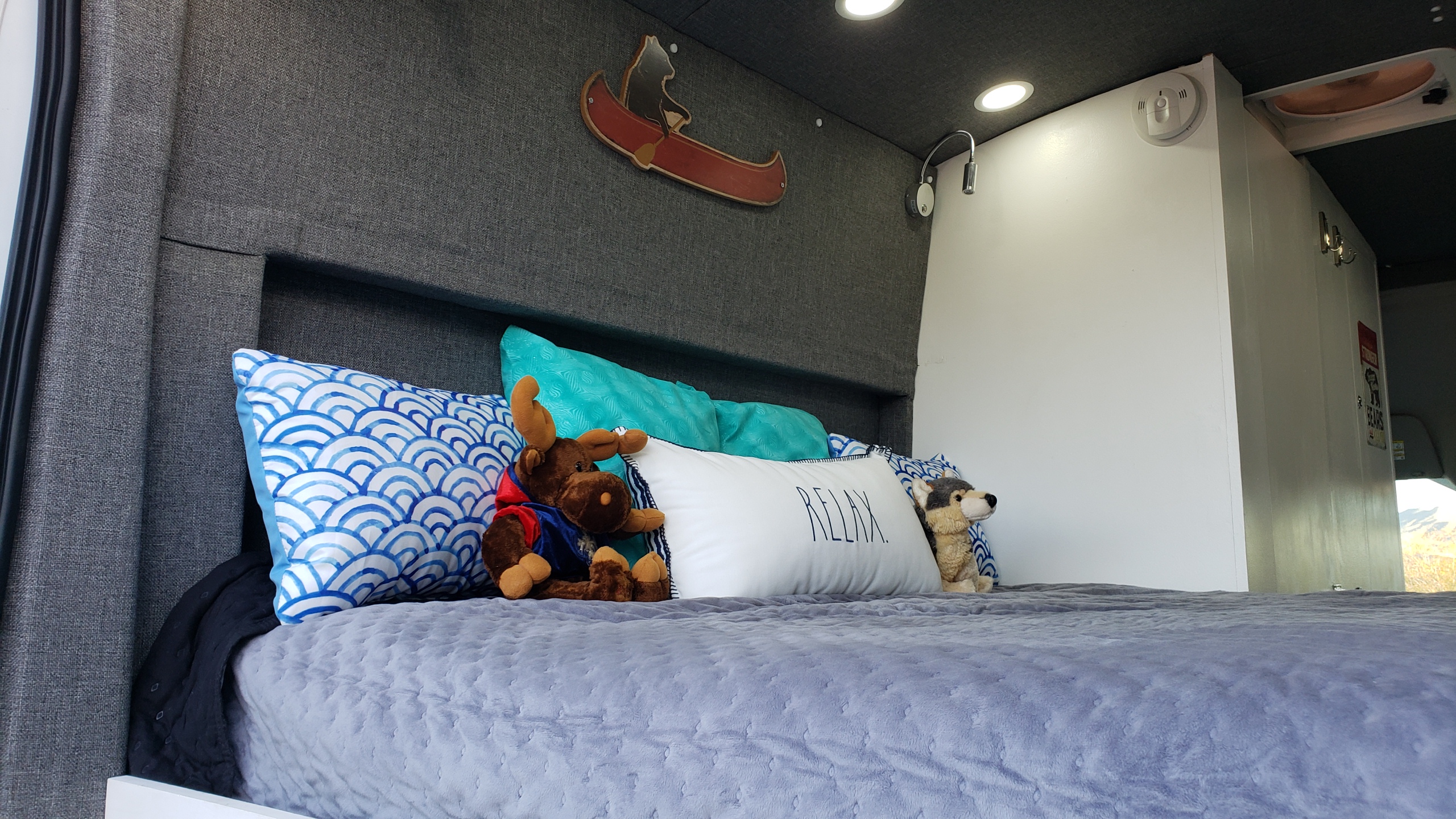 Relax in this cozy RV rental's comfortable bed with pillows & stuffed animals. Features include ceiling lights & wall decor.. Ford Transit Custom 2021