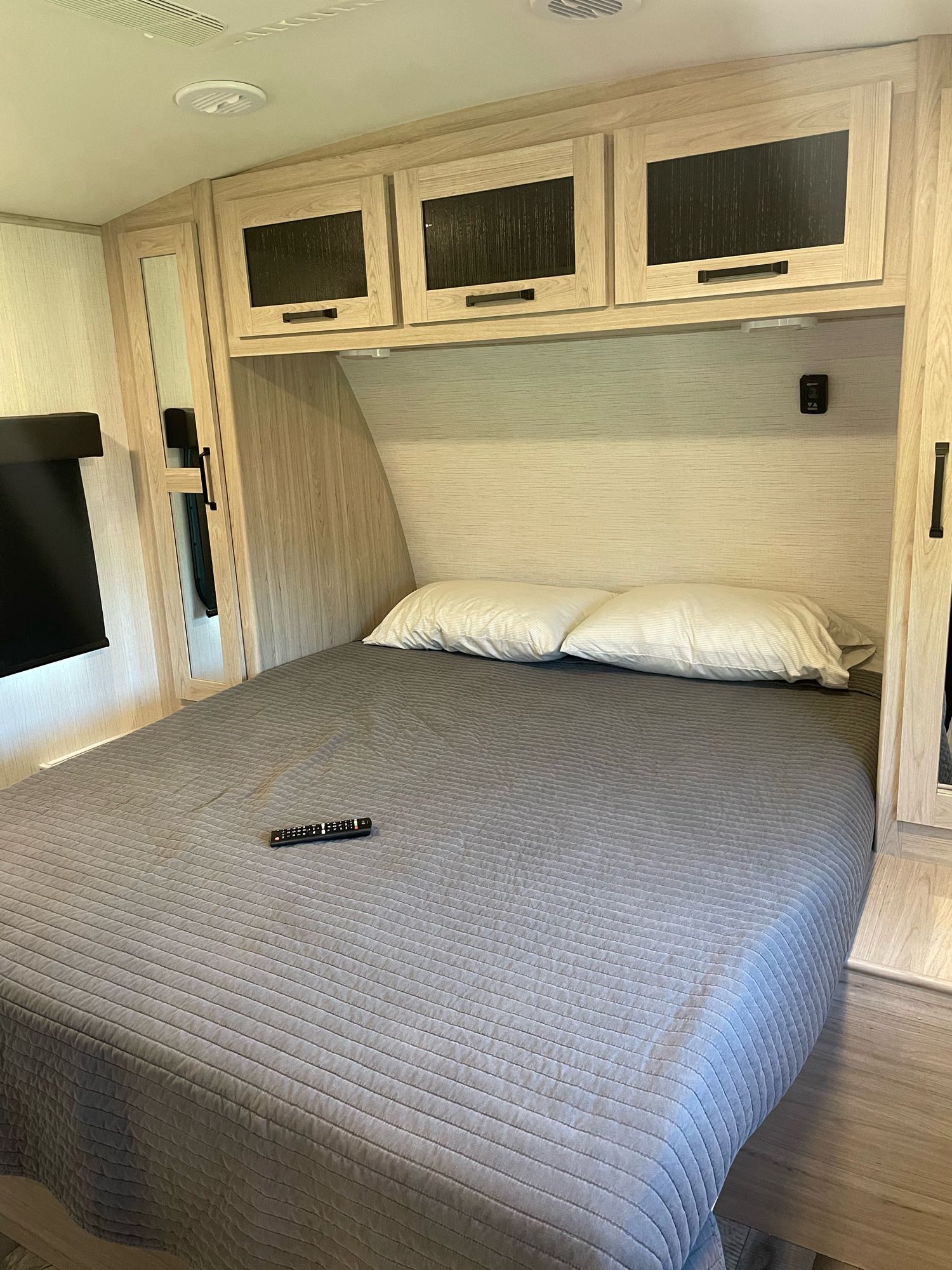 Experience comfort in this RV rental bedroom, featuring a full bed with gray bedding, sleek wood cabinets, and modern amenities.. Heartland Sundance 294BH 2022