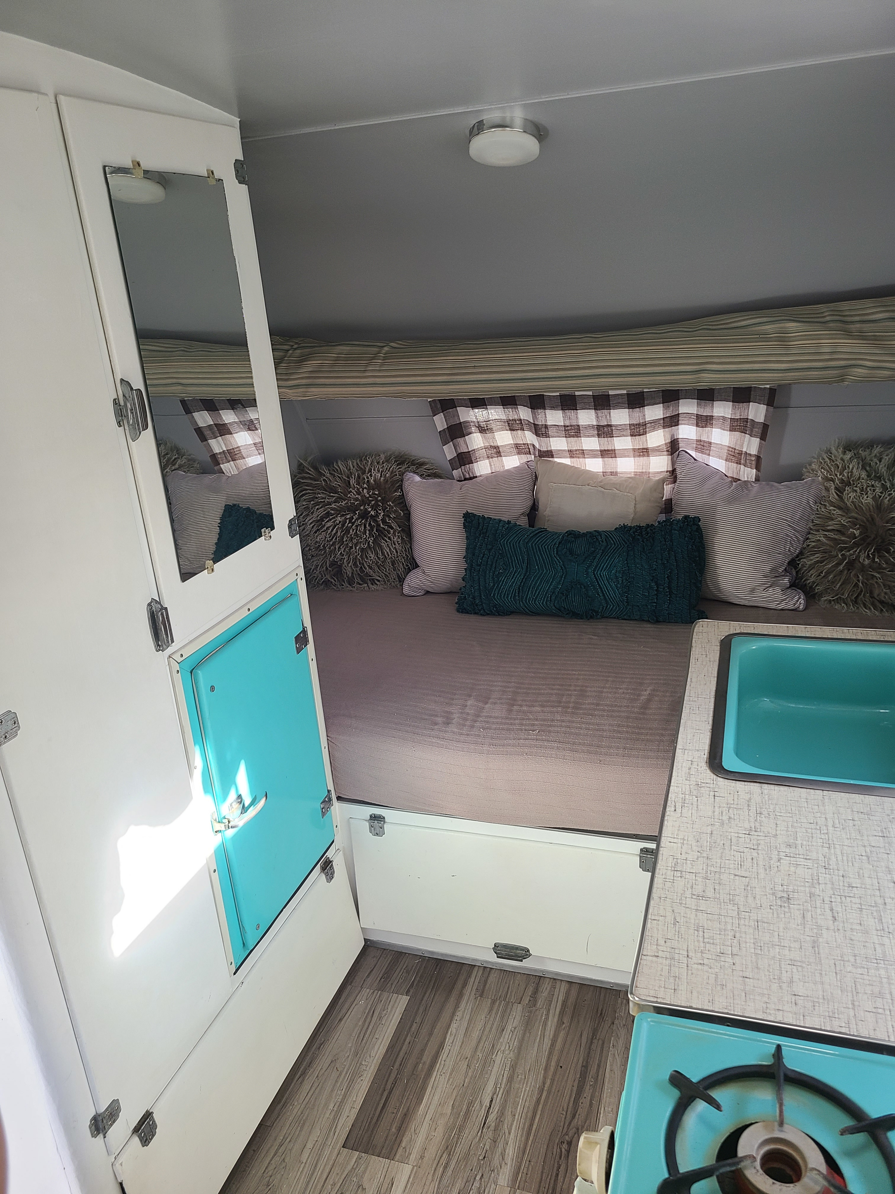 RV rental: Cozy camper interior, featuring a bed with pillows, teal sink, and stove setup.. Shasta 1500 1956