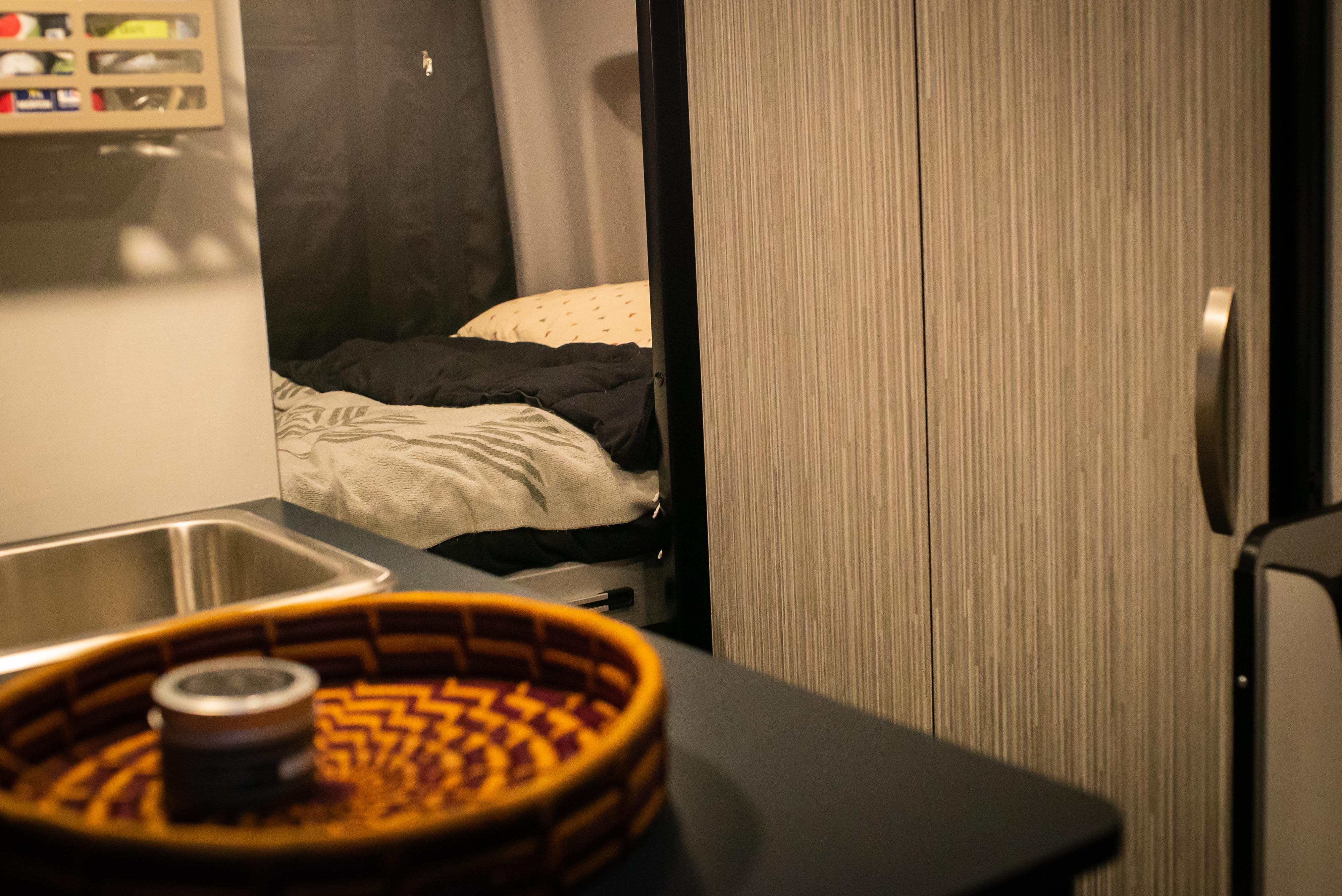 RV rental interior shows a compact kitchenette with sink, and a cozy bed area with blankets, highlighting practical amenities.. Winnebago Revel 2022