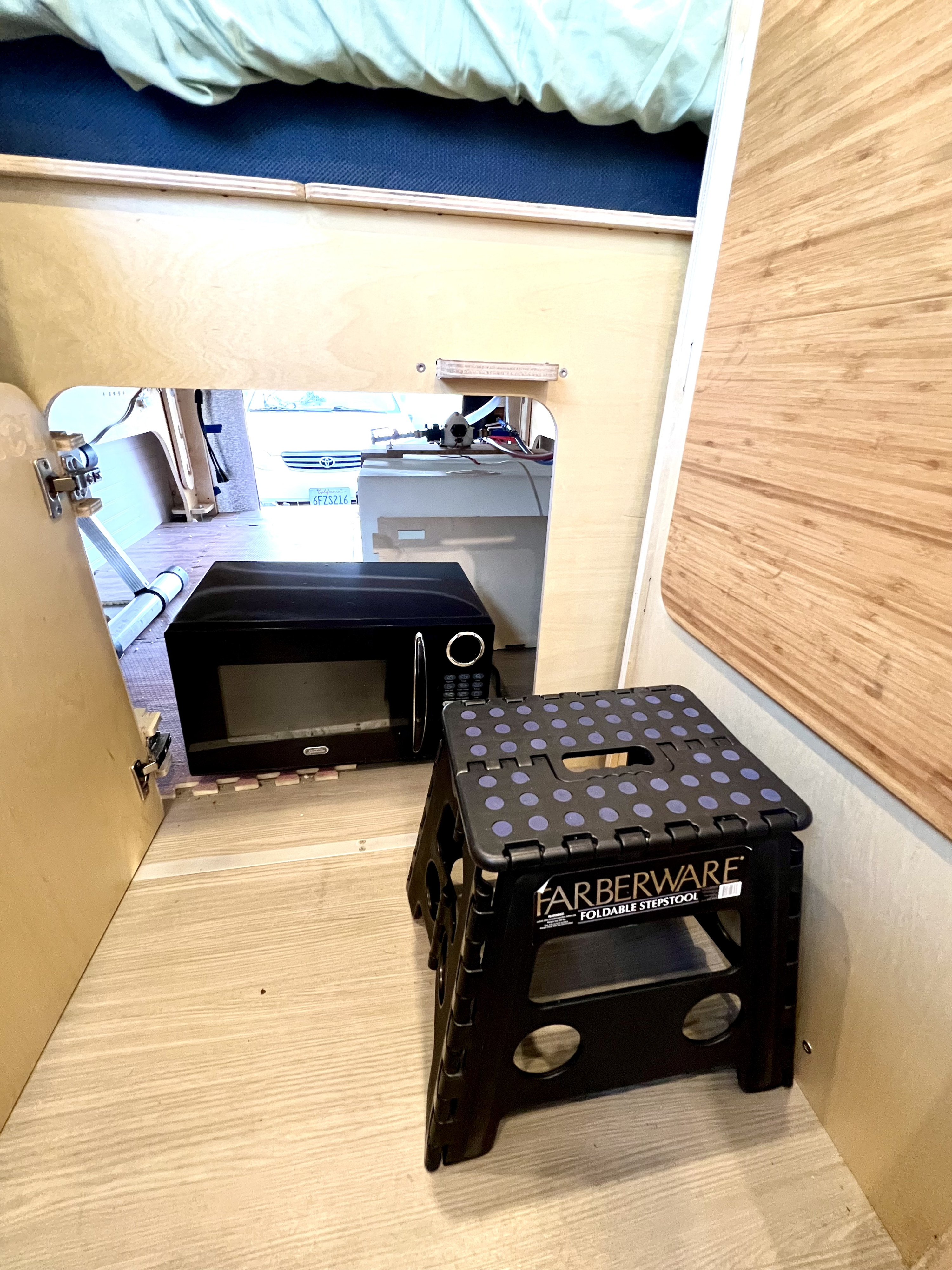 RV rental interior: Microwave & foldable step stool inside a compact camper setup with light wood walls.. Mercedes-benz Sprinter 2016