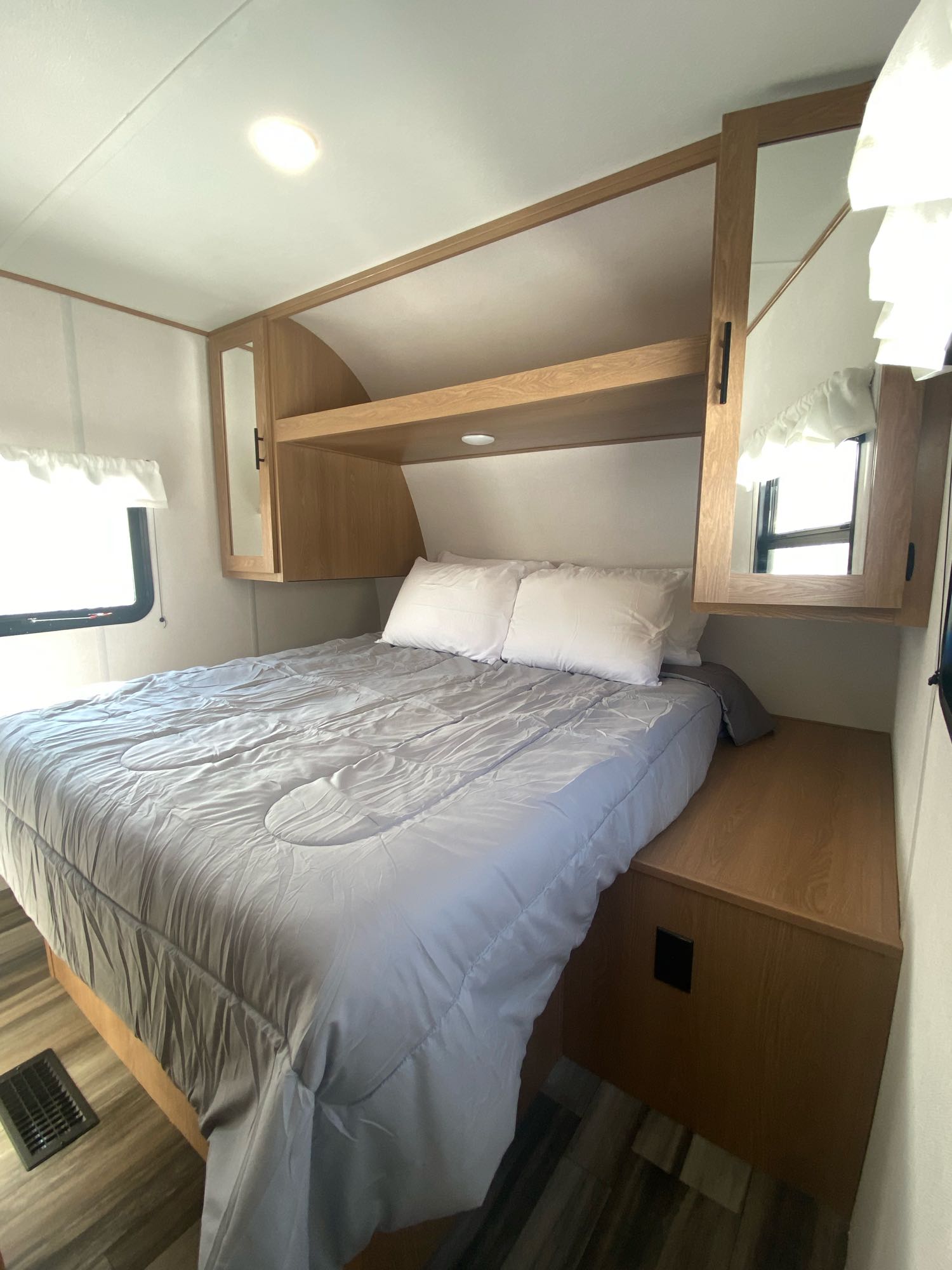 Inside an RV rental, a compact bedroom with a comfortable bed, overhead cabinets featuring mirrored doors, and windows.. Prime Time Avenger 26DBSLE 2022