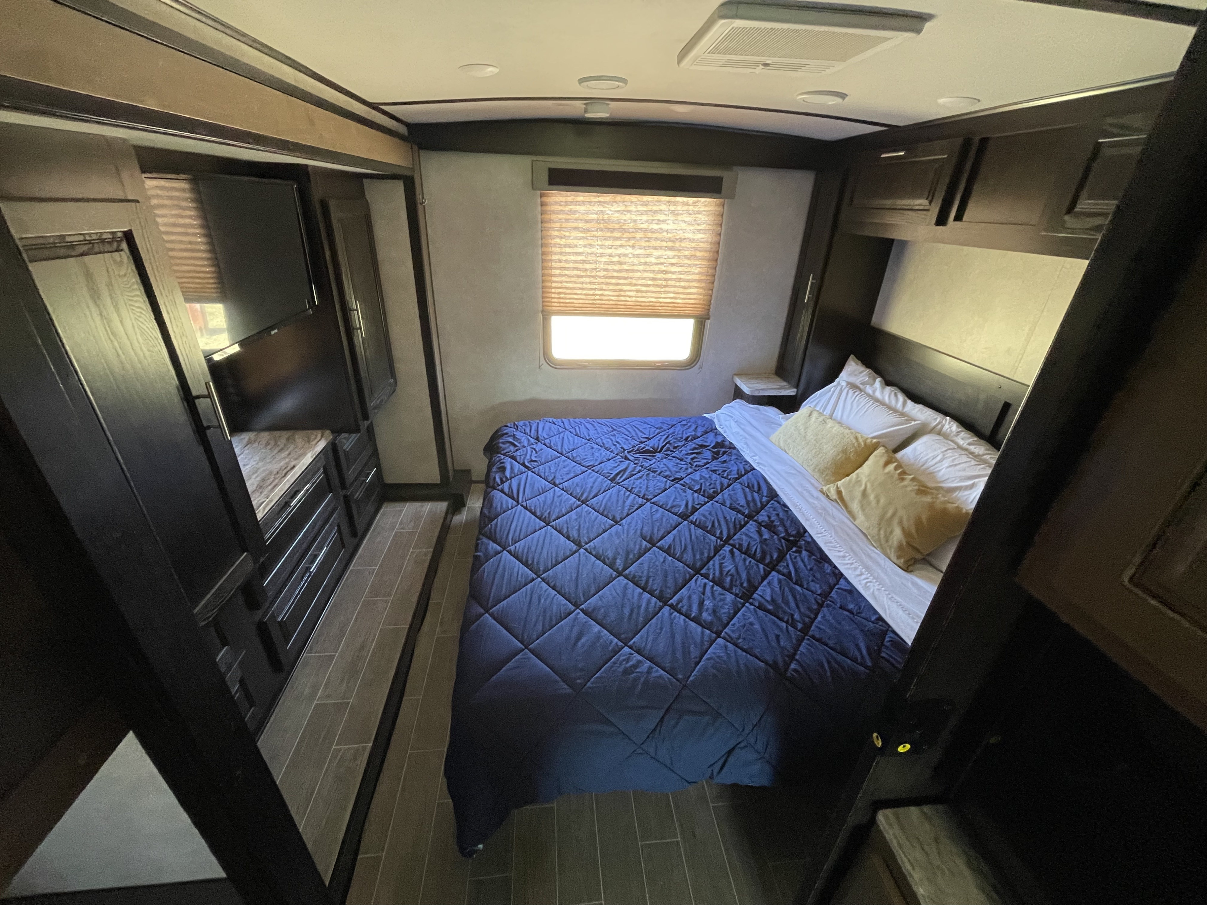 Cozy RV rental bedroom featuring a blue bed, mounted TV, window with blinds, and ample storage cabinetry.. FR3 FR3 Motorhome 2020
