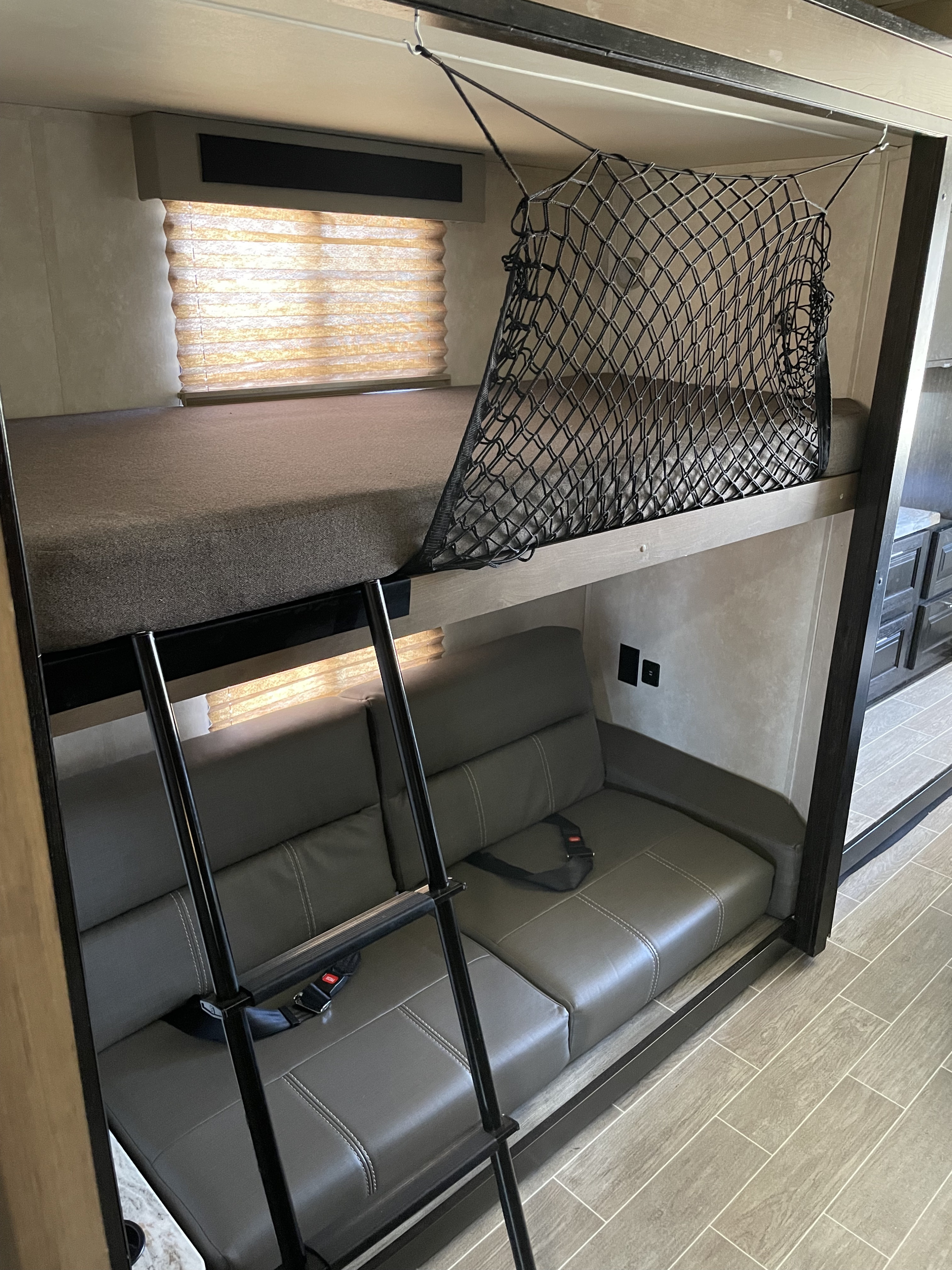 This RV rental features a bunk bed with a safety net, ladder, and a gray sofa below, offering compact living space.. FR3 FR3 Motorhome 2020