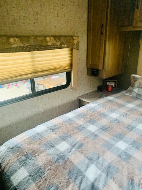 RV rental bedroom with a cozy plaid blanket on the bed, window, and wood cabinetry.. Forest River Coachmen Freelander 2016
