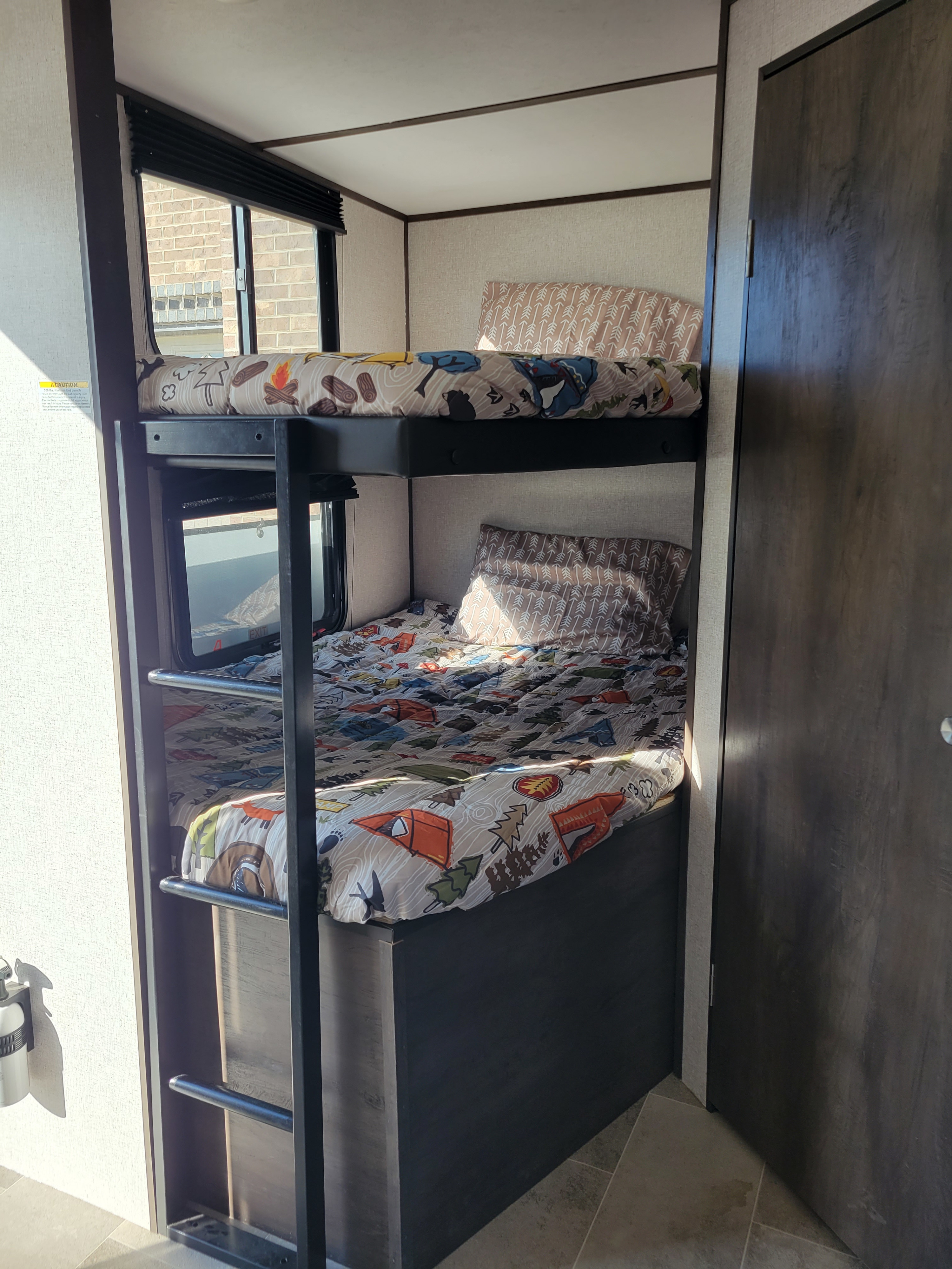 Inside an RV rental: two bunk beds with colorful camping-themed bedding, ladder, and window.. Dutchmen Coleman Lantern 2021