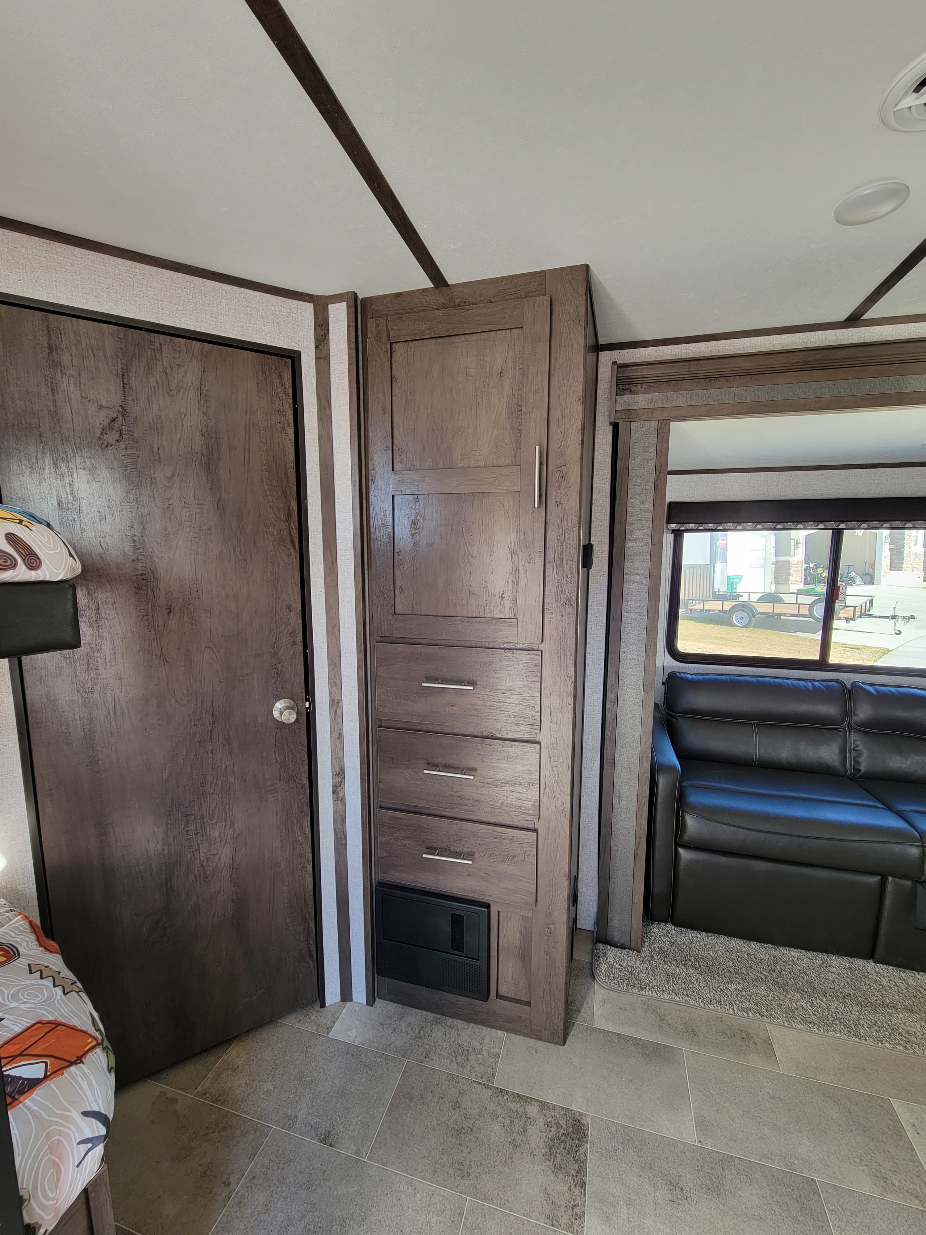 Spacious RV rental interior. Features dark wood cabinets, door, drawers, sofa, and a window. Light ceiling, grey tiled floor.. Dutchmen Coleman Lantern 2021