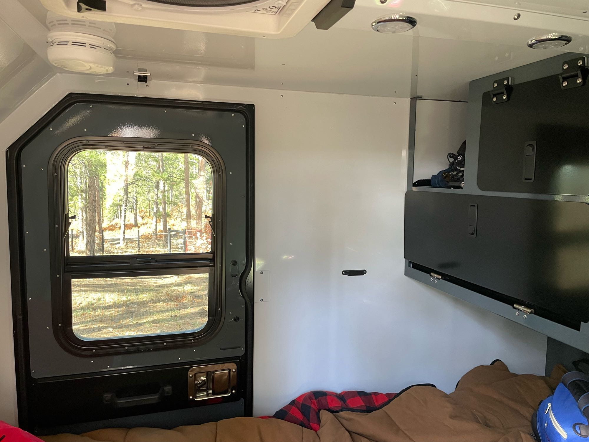 Cozy RV rental interior with a view of nature from the door, featuring a comfortable sleeping area and storage.. Off-Grid Trailers Pando 2.0 2022