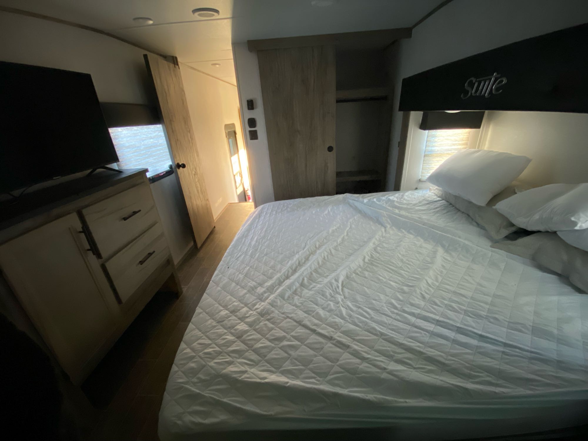 Inside an RV rental bedroom showing a bed with white bedding, TV on a dresser, and a sliding closet. A comfy suite on wheels.. Forest River Arctic Wolf 3770 Suite 2021