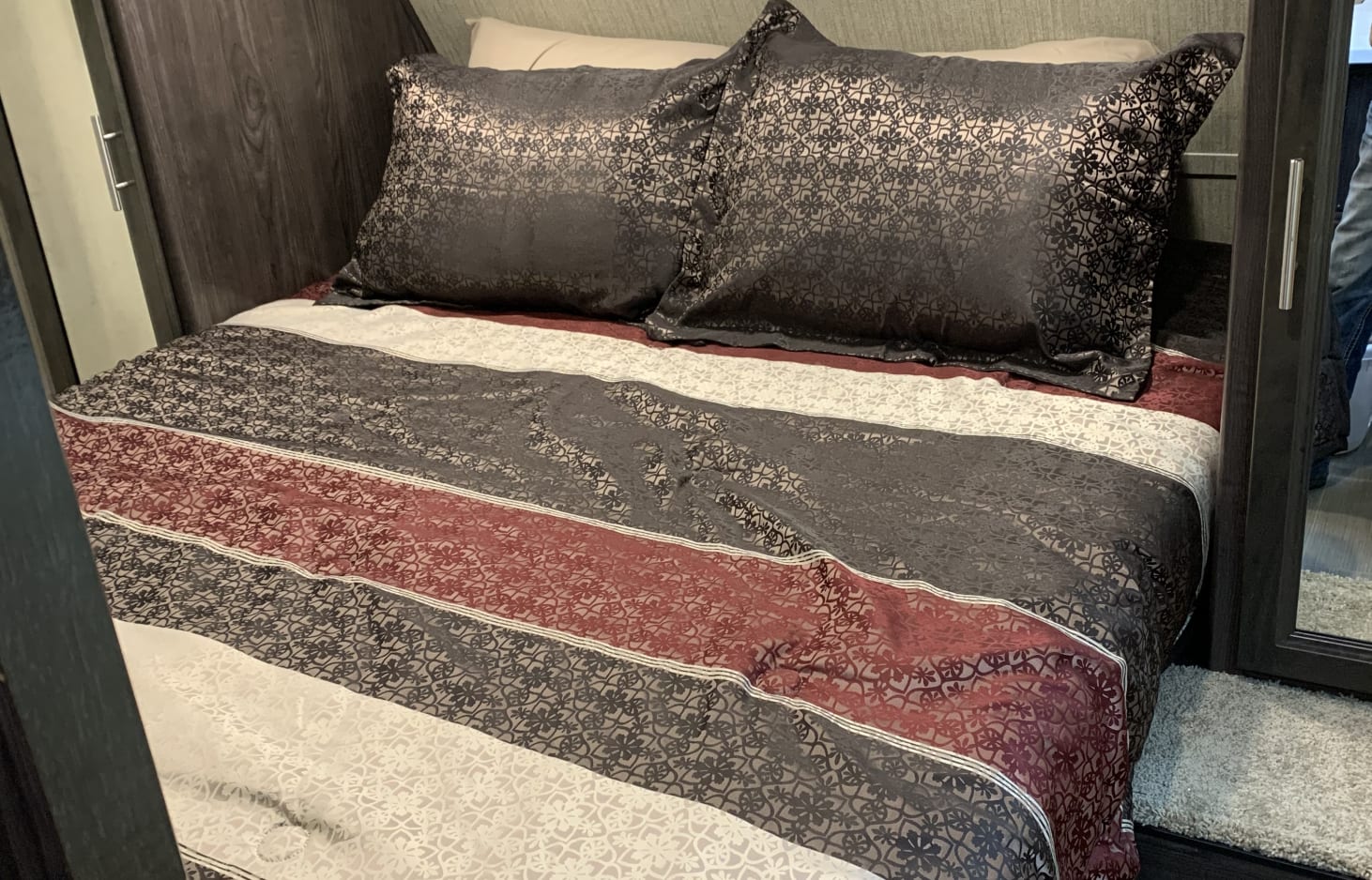 Cozy RV rental bedroom with striped, patterned dark gray, white & burgundy bedding and matching pillows.. Starcraft Autumn Ridge 2020