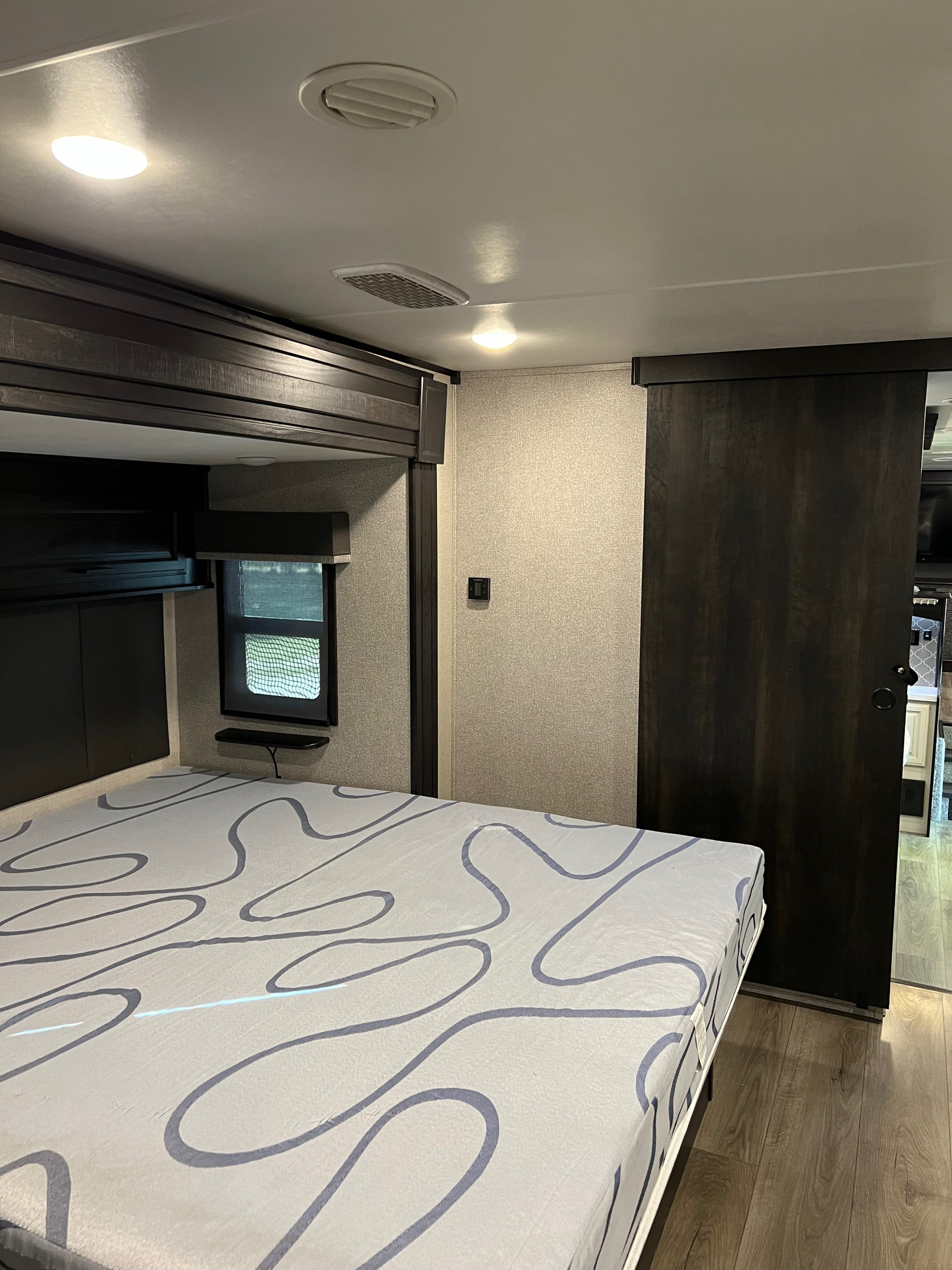 Cozy RV rental bedroom interior, featuring a patterned bed, overhead storage, and sliding door for travel comfort.. Open Range 373RBS 2021