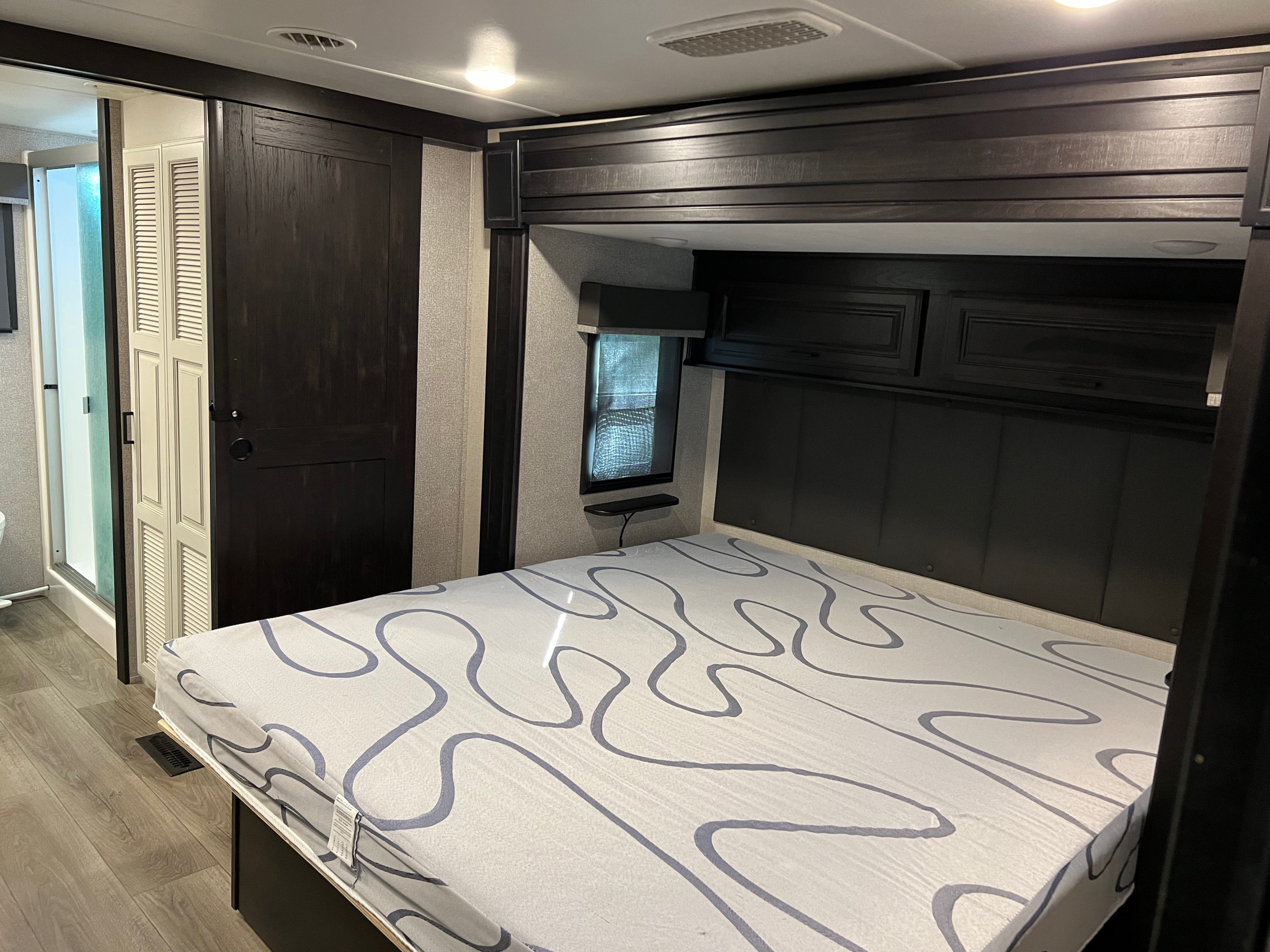 RV rental bedroom with a large bed, dark wood built-ins, and a louvered closet/bathroom door.. Open Range 373RBS 2021