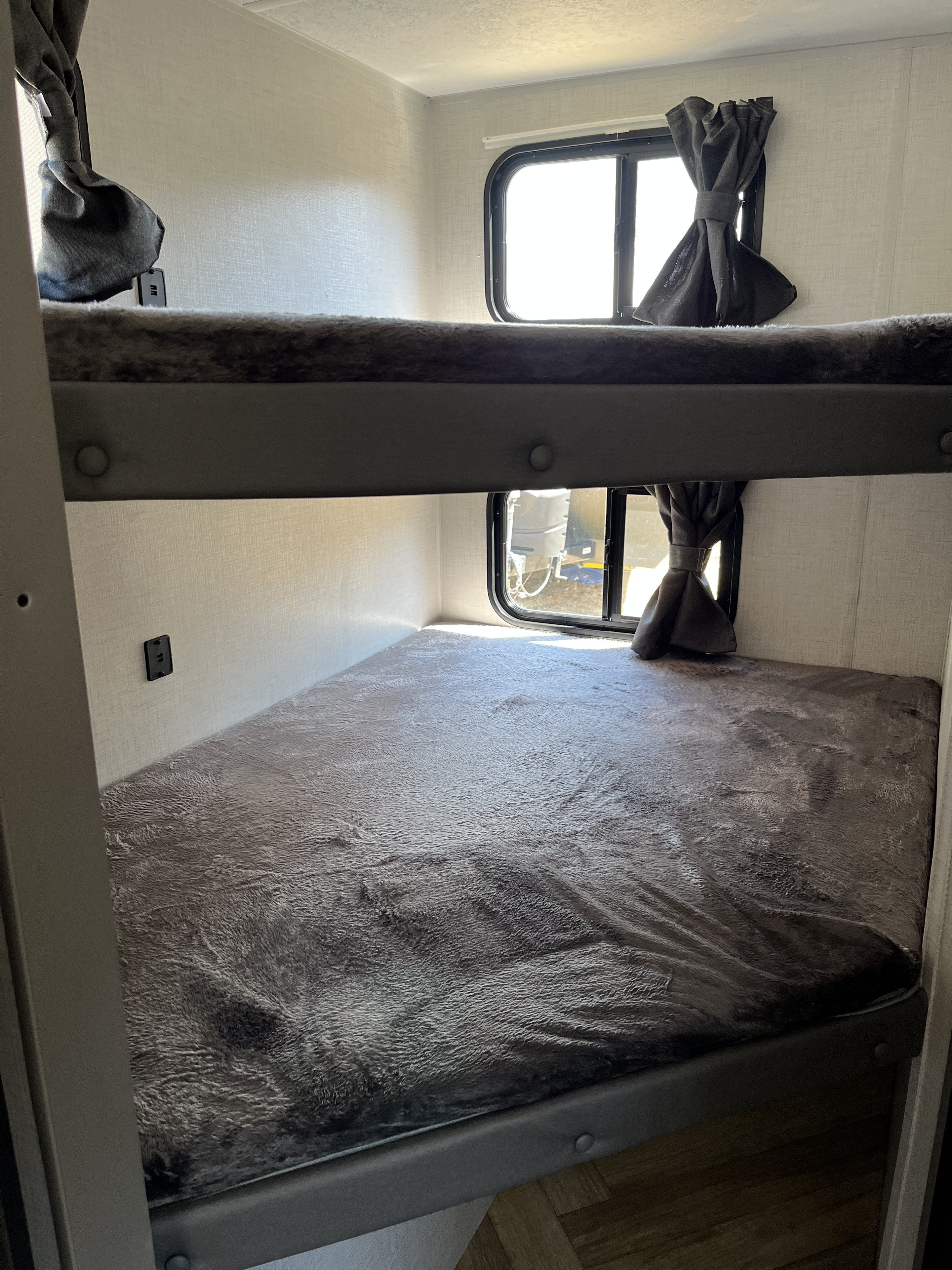 View of two bunk beds inside an RV rental, each with a soft gray blanket, and windows beside them.. Forest River 1650BHK 2022