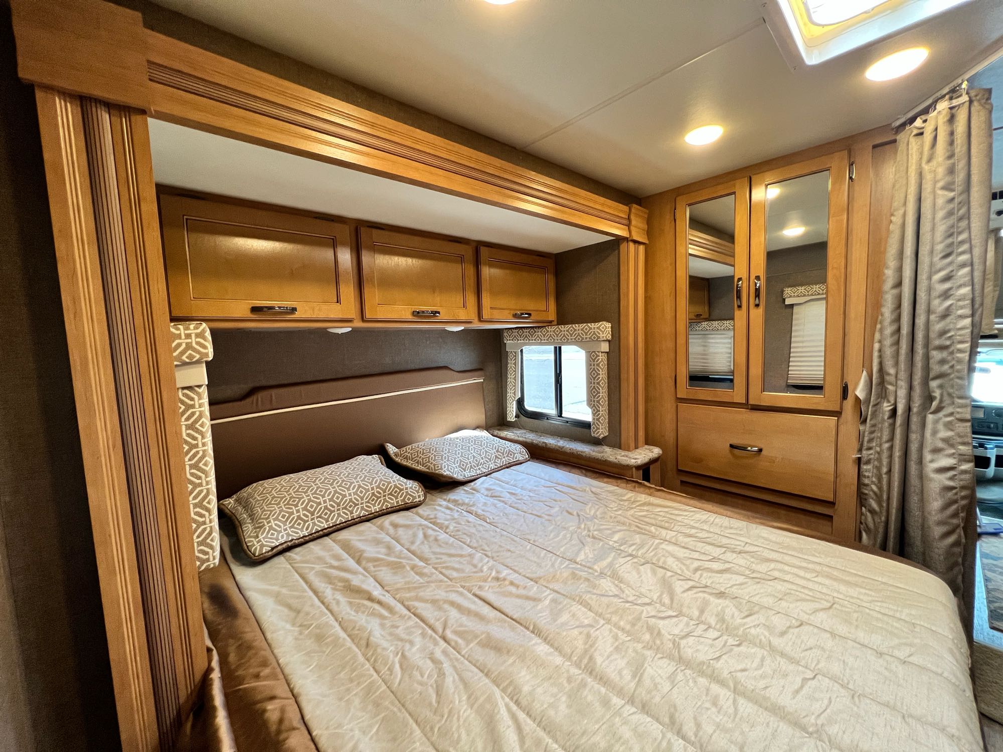 Comfortable RV rental bedroom featuring a bed, overhead cabinets, mirrored wardrobe, and recessed lighting. Cozy RV interior.. Thor Freedom Elite 2017