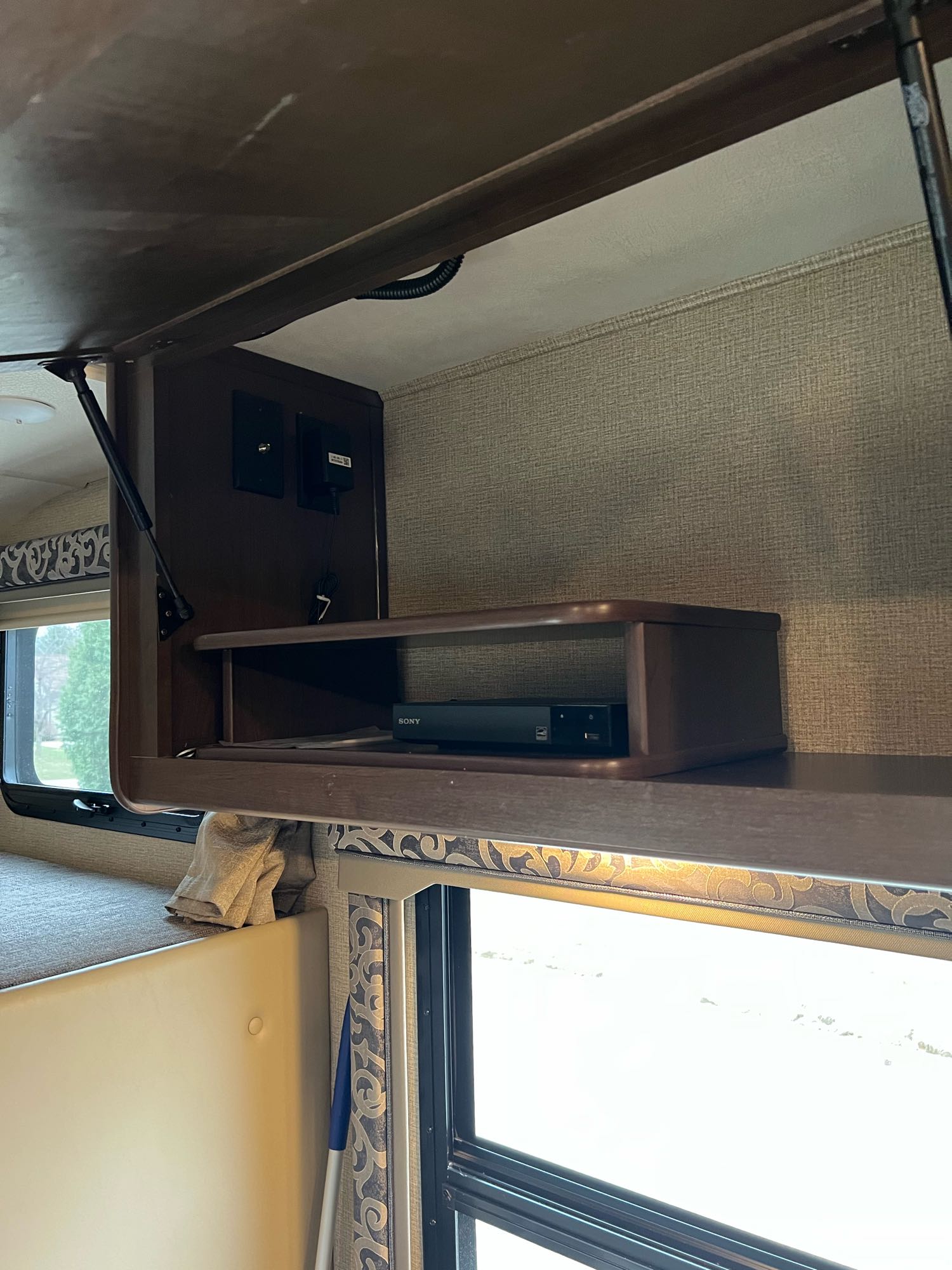 Inside an RV rental: an open overhead cabinet with a Sony media player shelf and connections, beside a bunk and window.. Thor Motor Coach Four Winds 2018