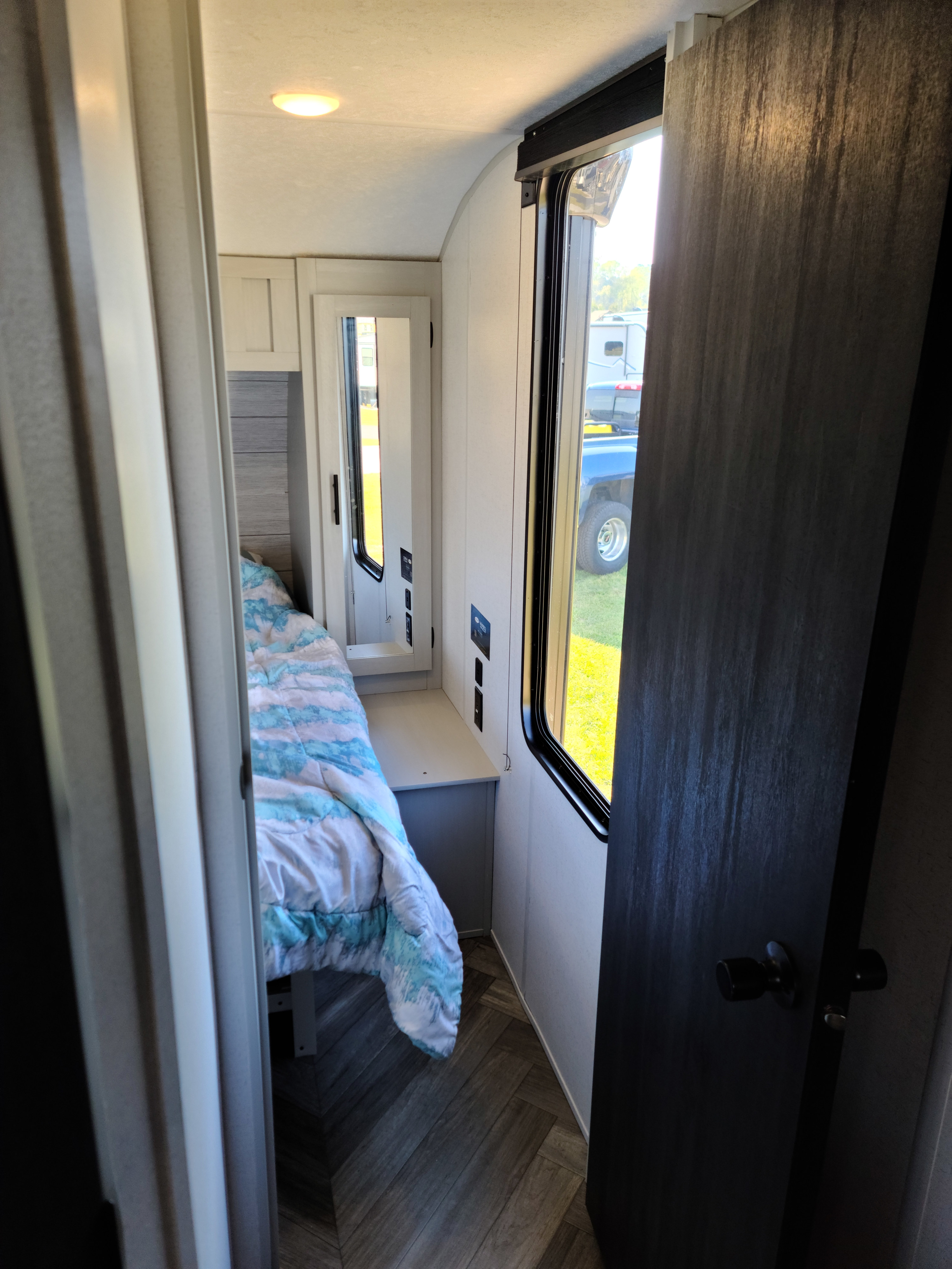 Inside this cozy RV rental: a compact bedroom with a bed, window, nightstand, and wood-look flooring.. Forest River Salem 2022