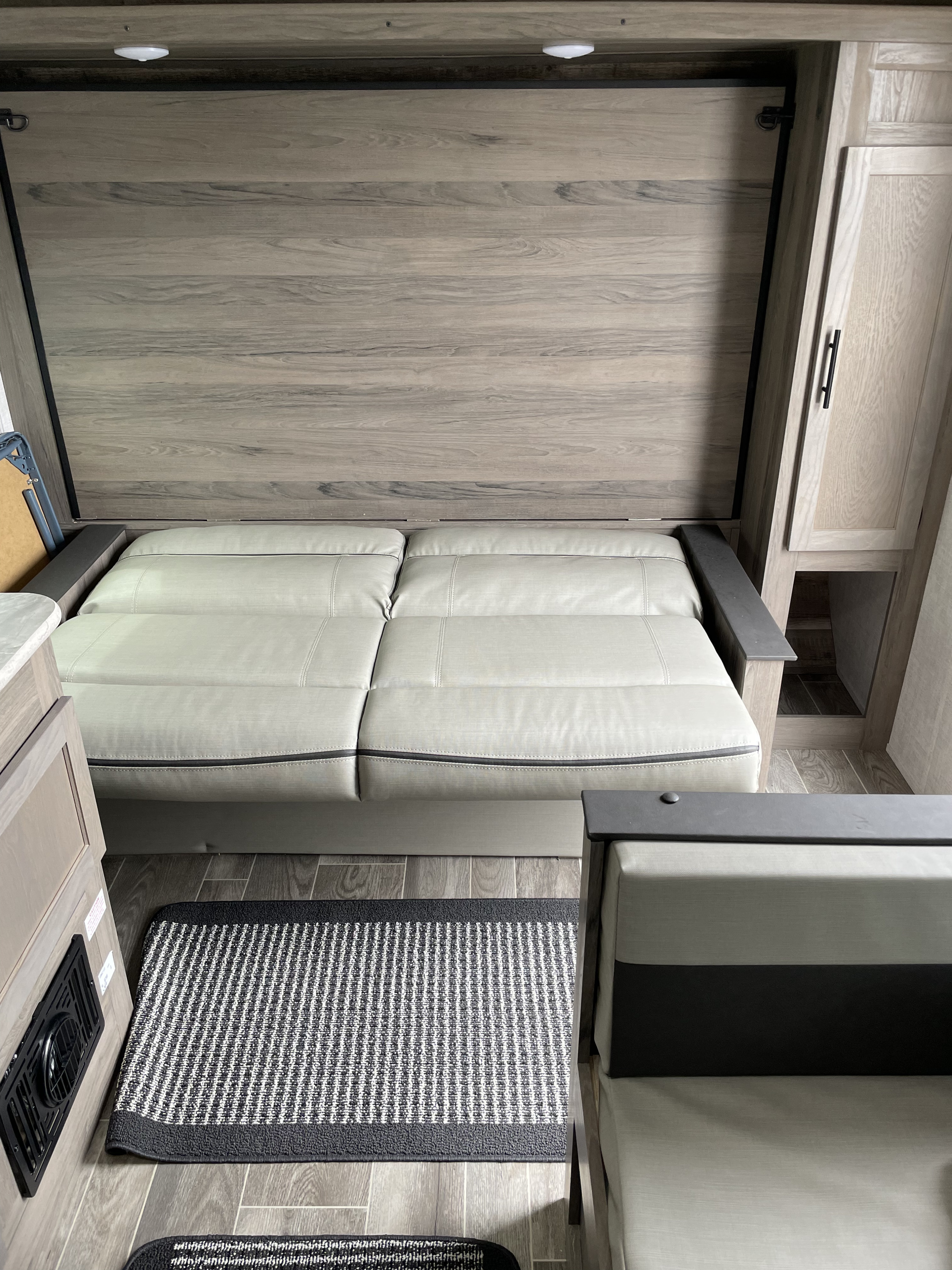 This RV rental showcases a light gray convertible sofa bed against wood-look panels, complete with modern cabinets and a striped rug.. Gulfstream Enlighten 19BH 2022