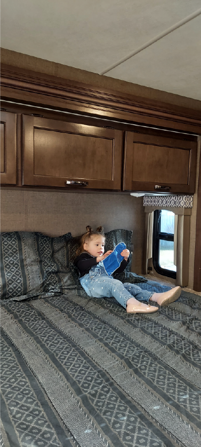 Child relaxes comfortably in an RV rental bedroom, holding a blue item.. Thor Freedom Elite 2017