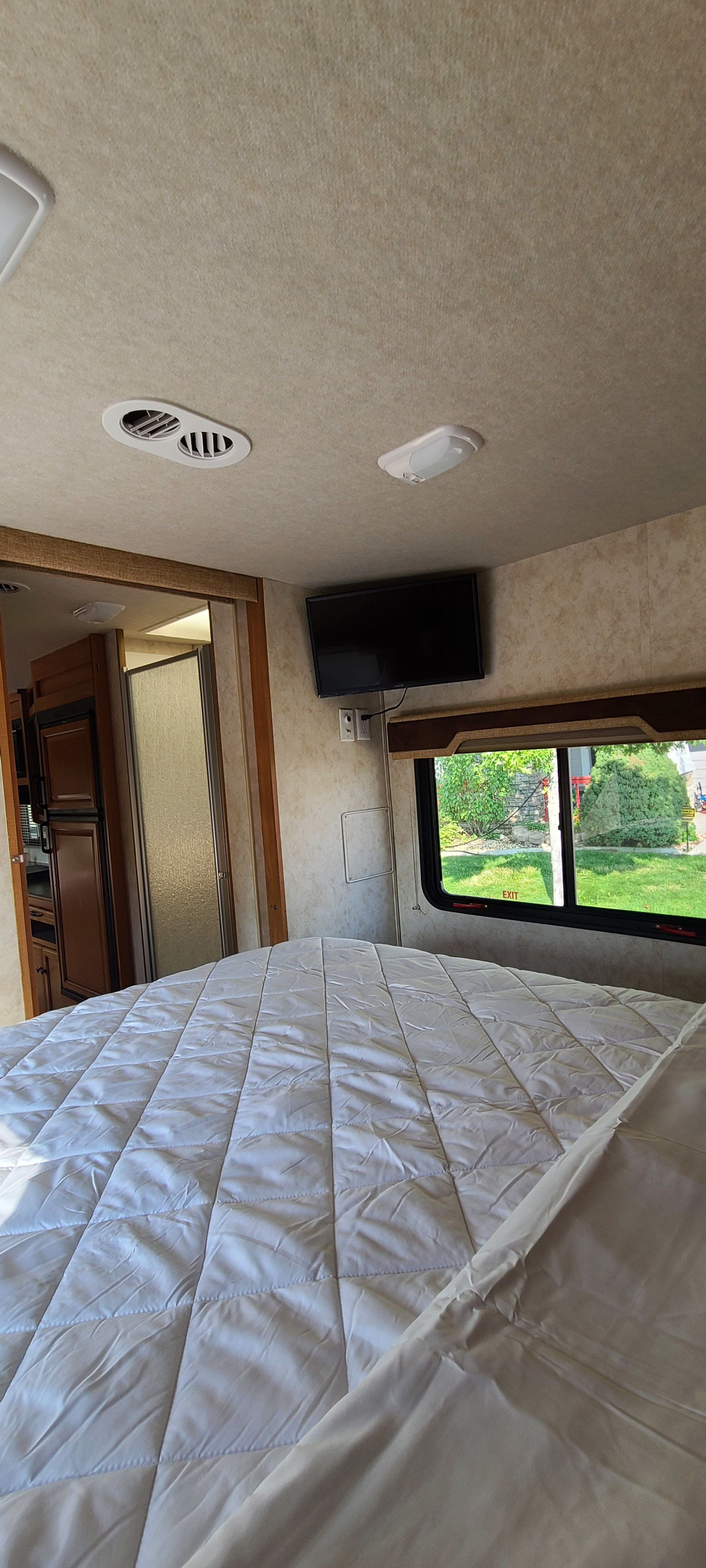 Cozy RV rental bedroom: Quilted bed, wall-mounted TV, window with outdoor view, and adjacent compact living space.. Jamboree Jamboree Motorhome 2011