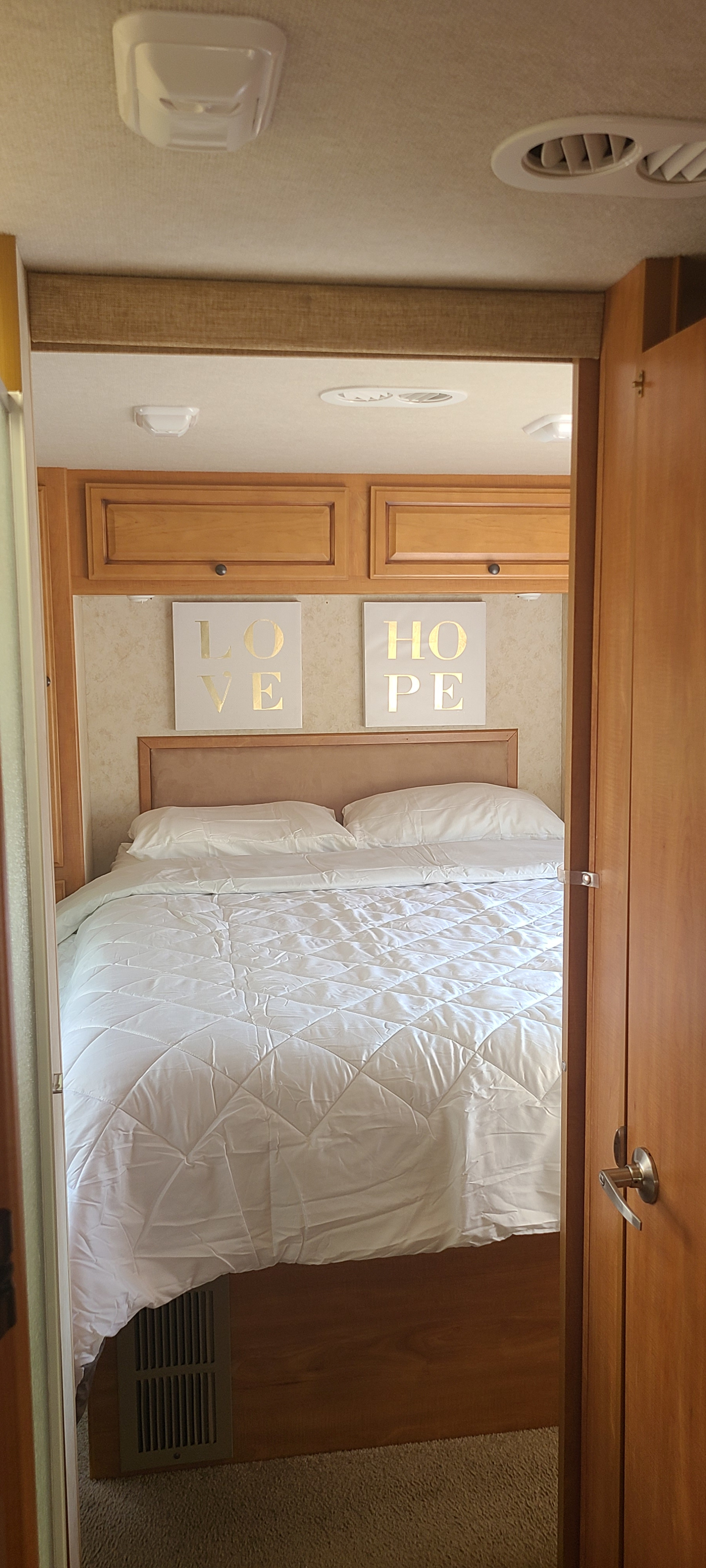RV rental bedroom features a comfy bed with white bedding, "LOVE" and "HOPE" signs, cabinets, and ceiling vents.. Jamboree Jamboree Motorhome 2011