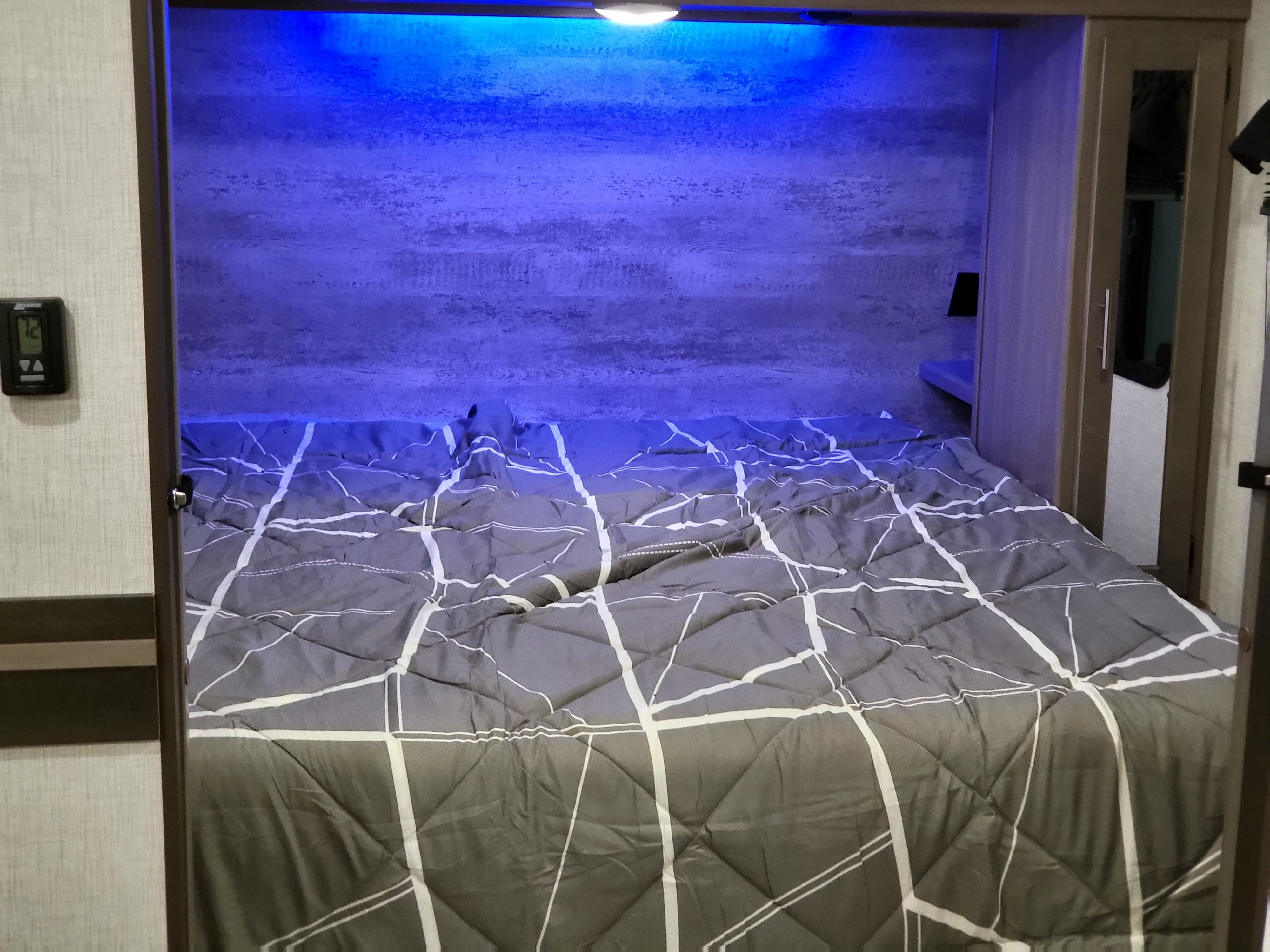 Cozy RV rental bedroom featuring a grey patterned bed, blue mood lighting above, and a thermostat (72°F) on the wall.. Crossroads RV Sunset Trail Super Lite 2022