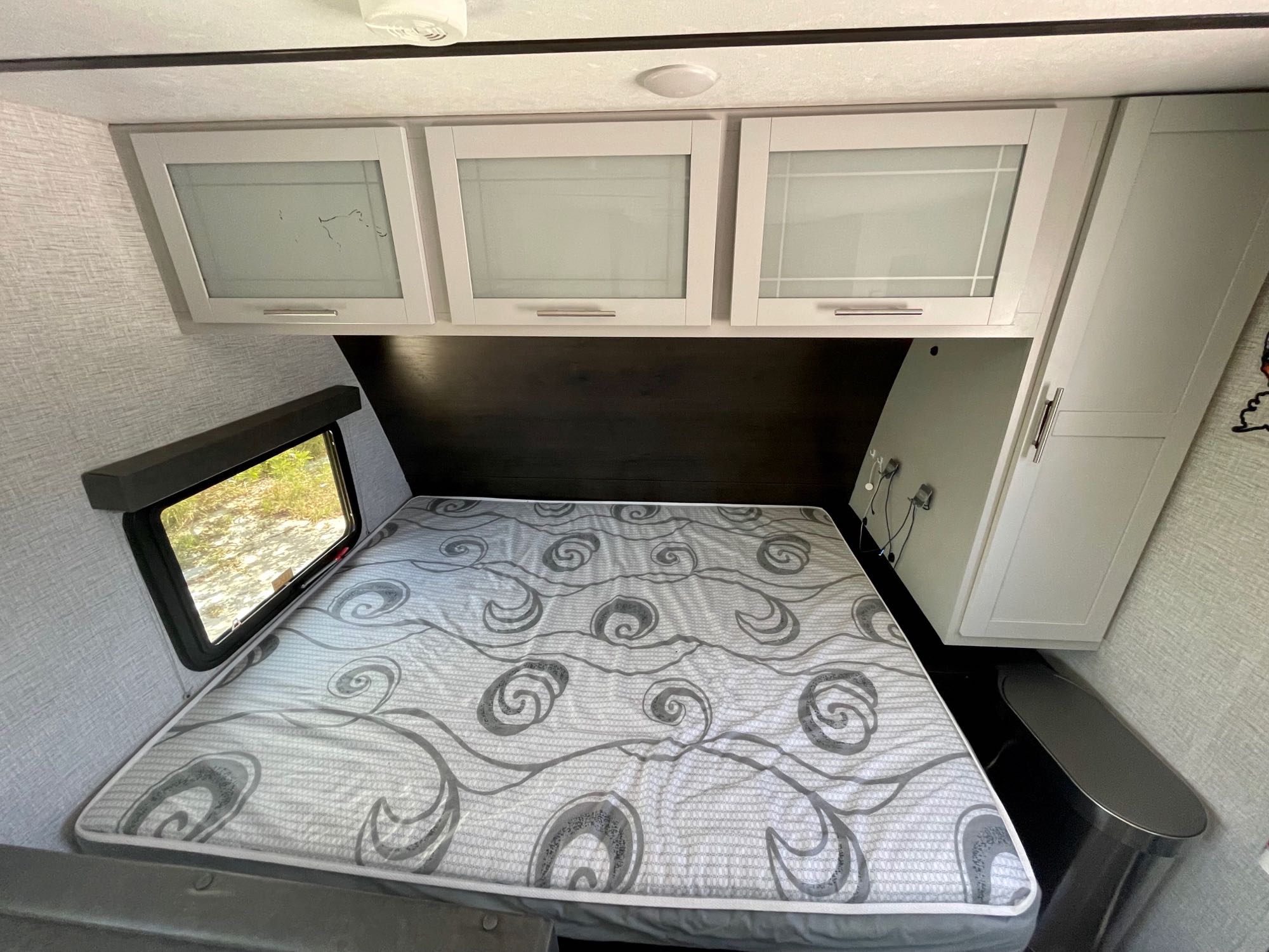 Cozy RV rental bedroom featuring a patterned mattress, overhead storage cabinets, and a window for scenic views during travel.. Keystone RV Bullet Crossfire 2021