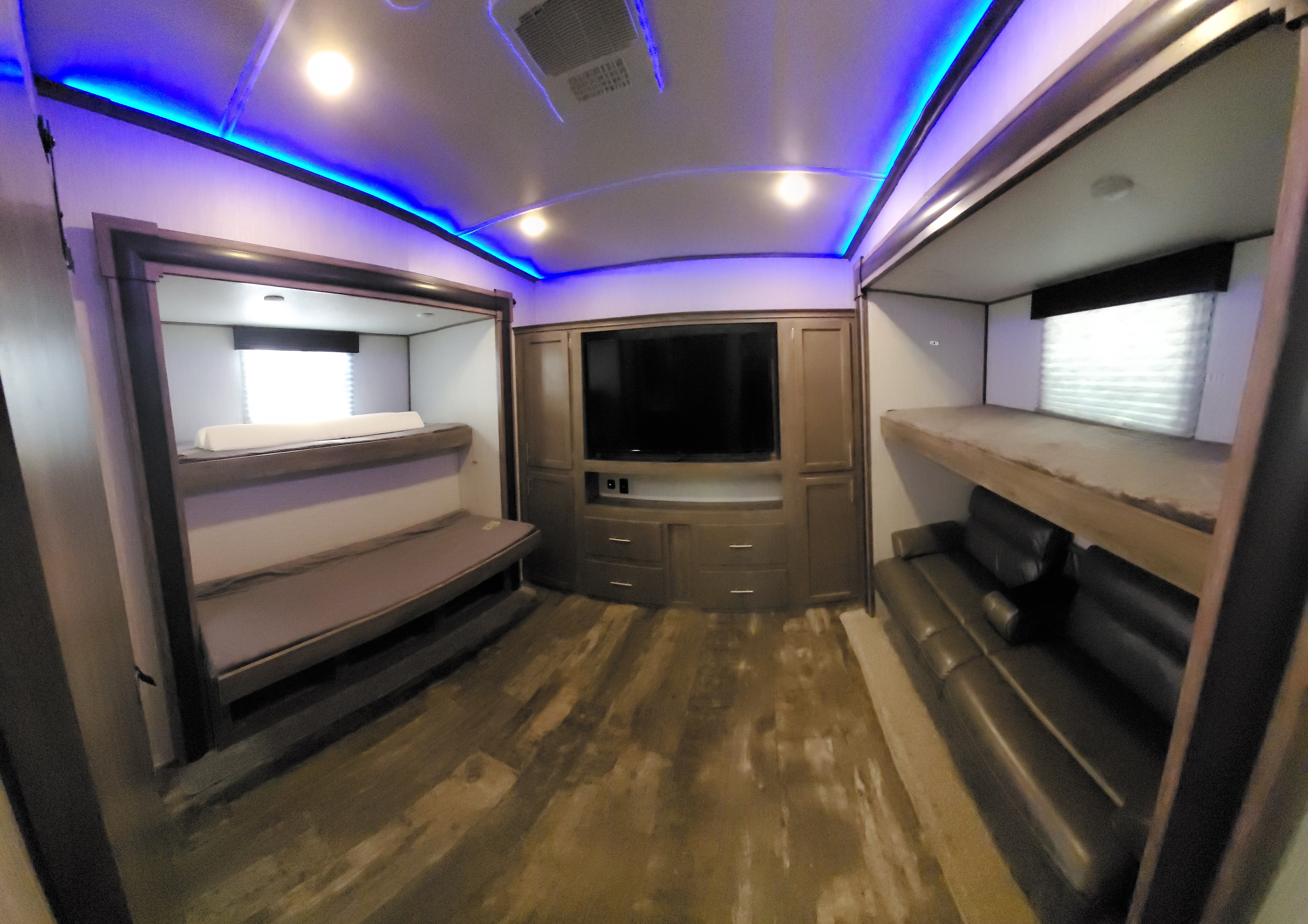 An RV rental interior with bunk beds, sofa, and entertainment center, illuminated by cool blue ambient lighting.. Forest River Sabre 2020