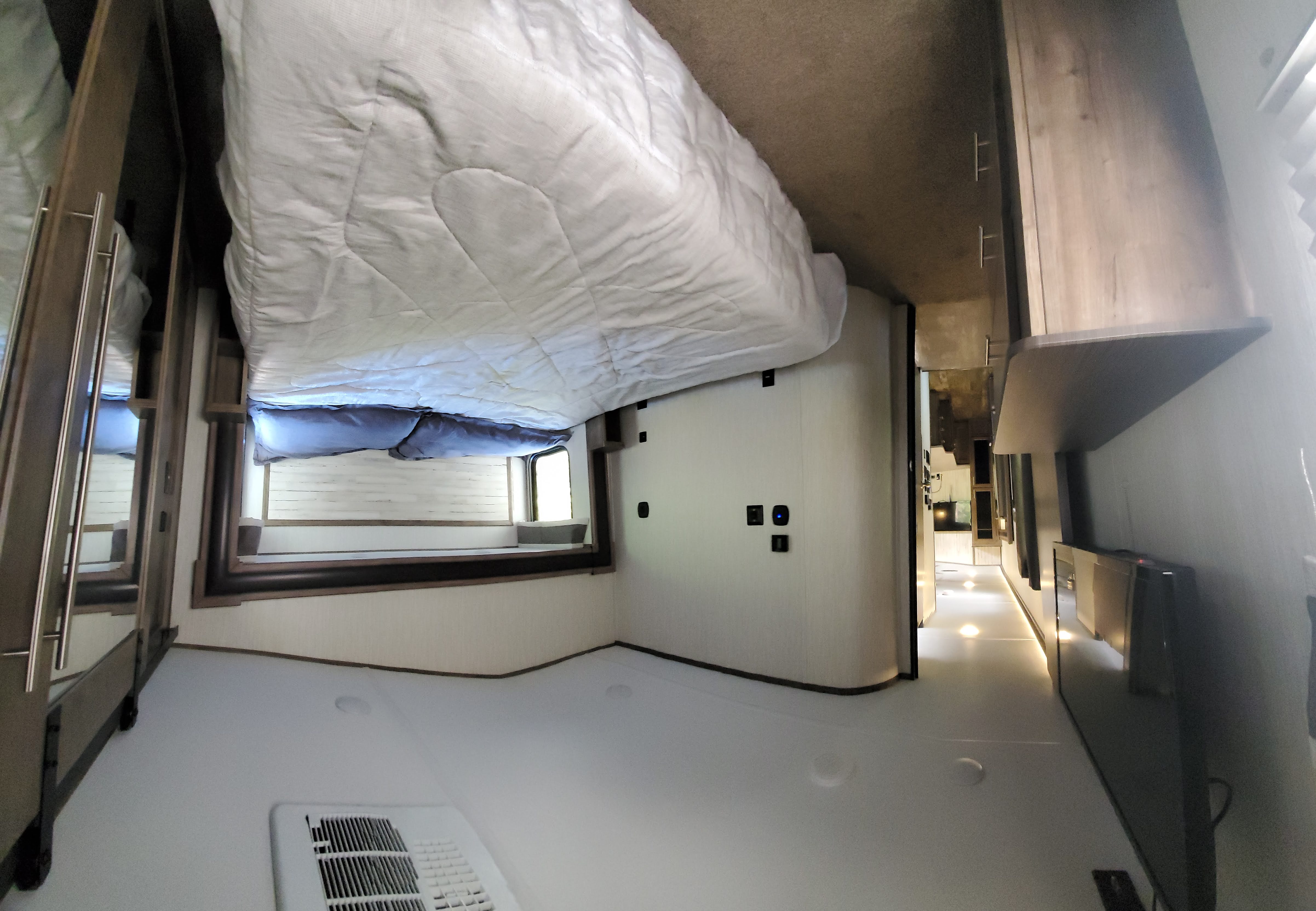 An RV bedroom with a white comforter on the bed, and a brightly lit hallway extending away. This modern space is ready for your rv rental adventure.. Forest River Sabre 2020